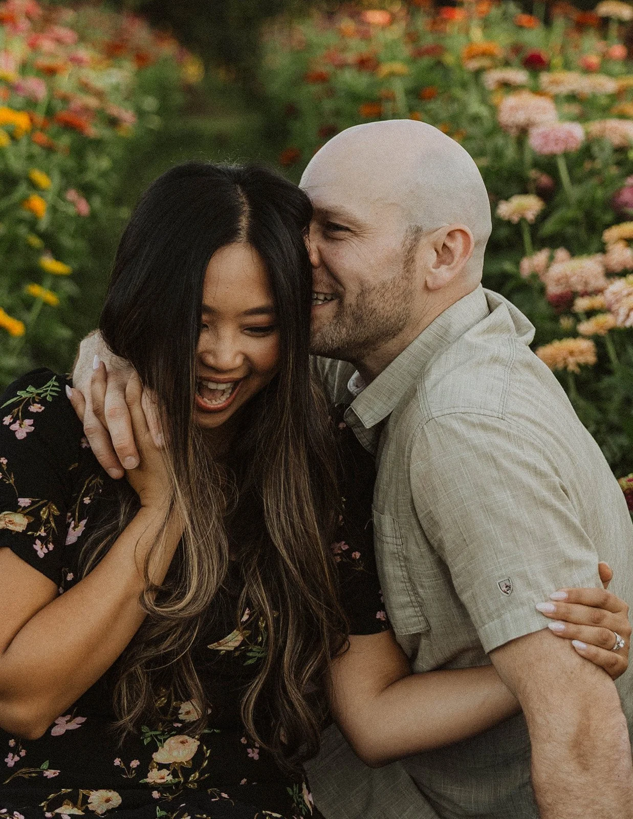 Close-up engagement portrait of a couple sharing a playful moment among colorful flower gardens.