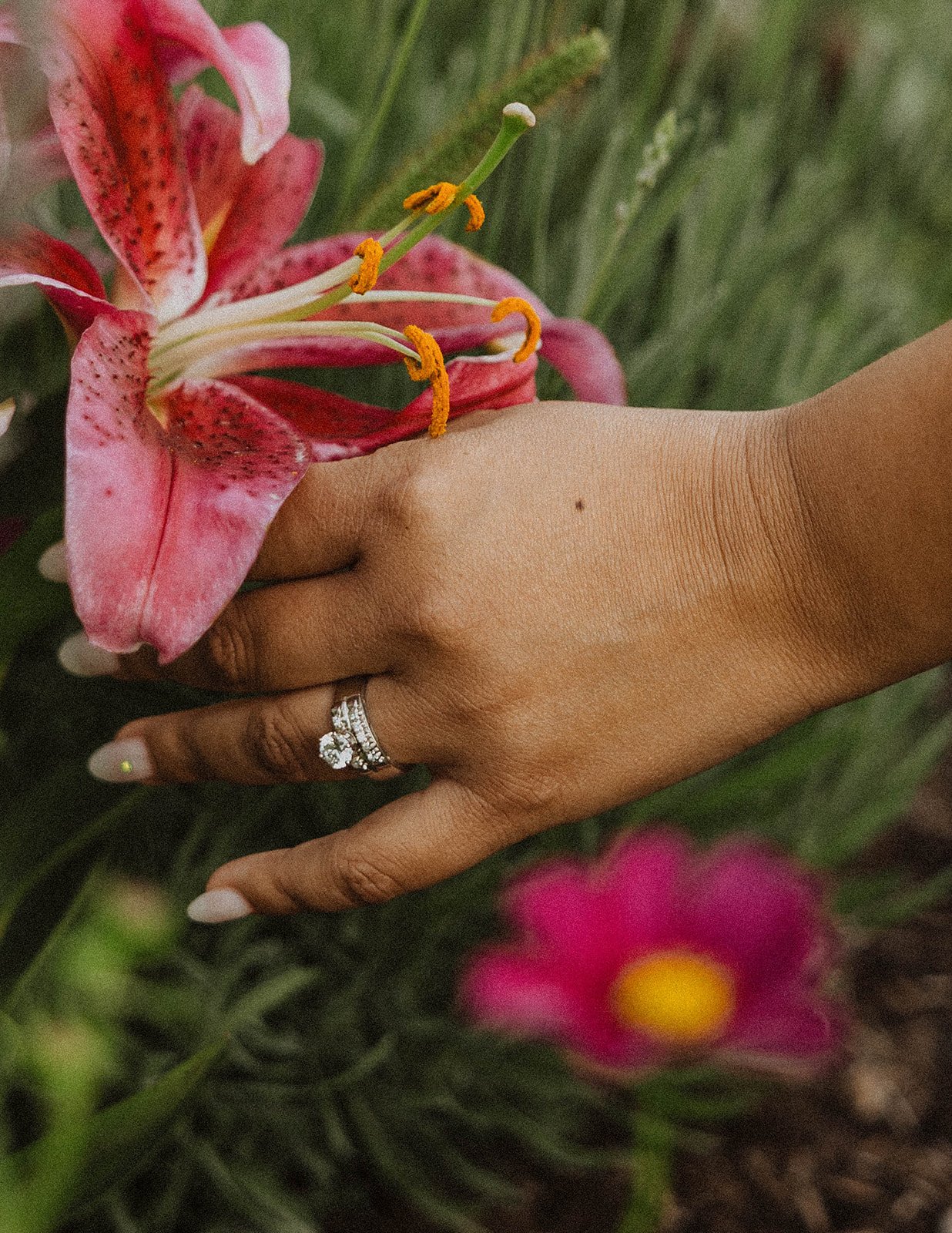 Close-up of an engagement ring beside a pink lily bloom during a flower field engagement session.