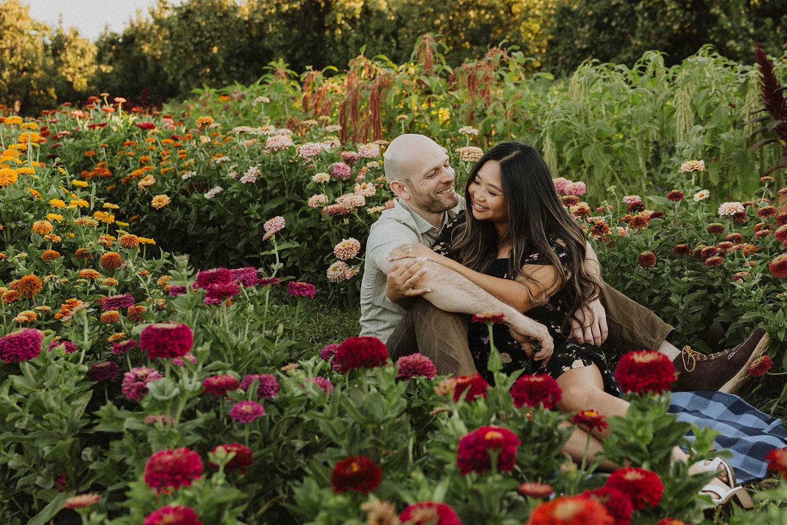 Couple relaxing together on a blanket among blooming zinnias during a flower farm engagement session.