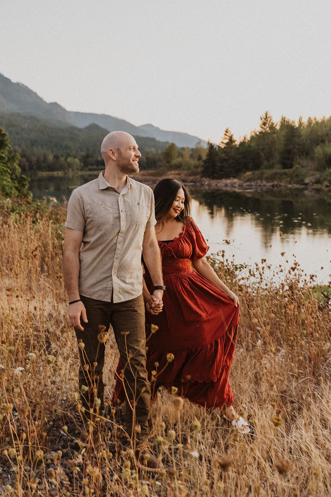 Couple walking hand in hand beside the river with mountain views and soft evening light near Mt Hood.