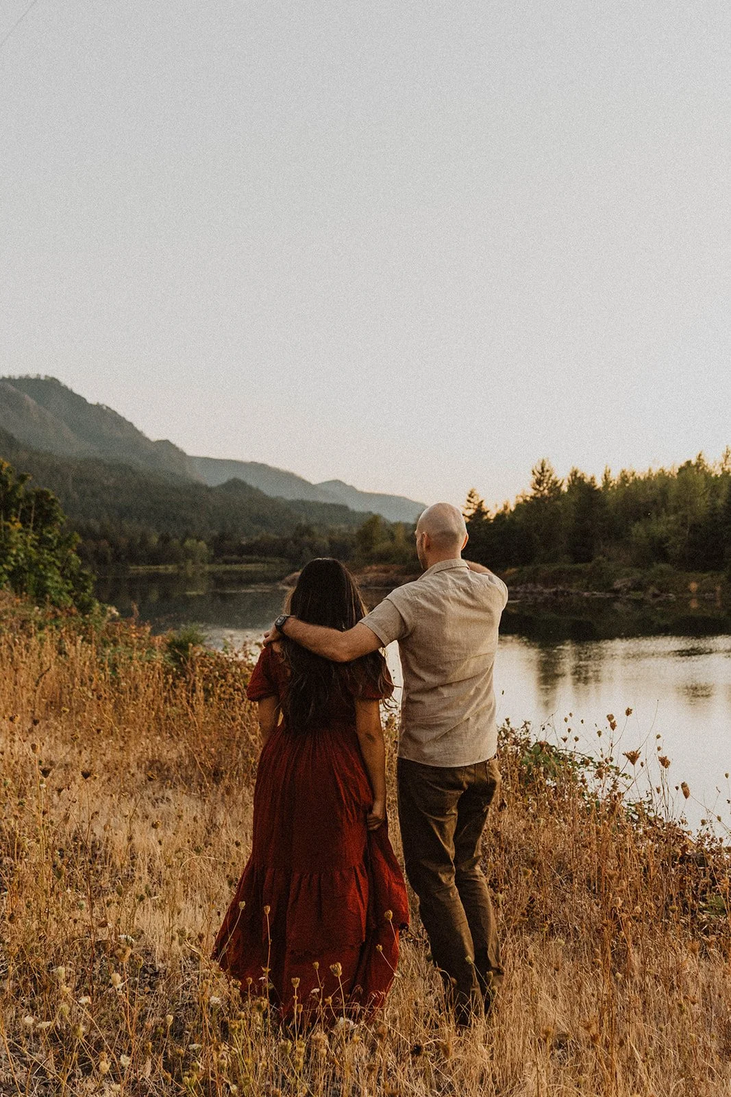 Couple standing together overlooking a peaceful mountain lake during a romantic engagement photo session.
