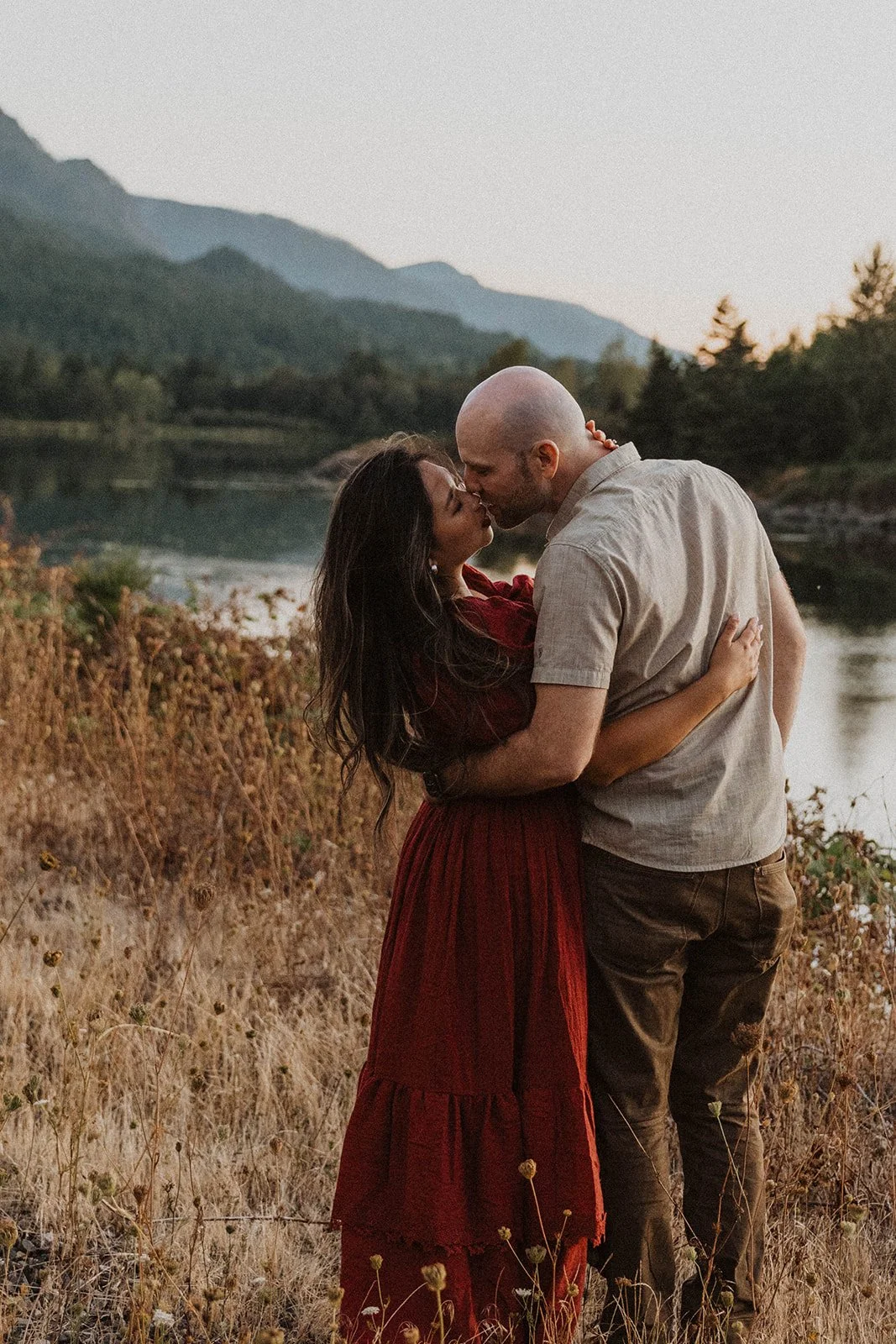 Couple sharing a kiss along a lakeshore during a mountain engagement session at golden hour.