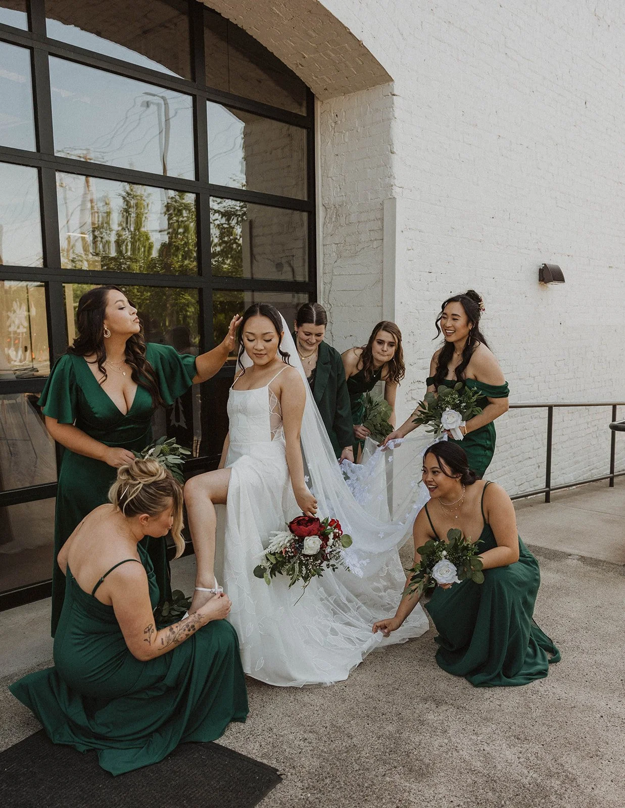 Bridesmaids help adjust the bride's dress and veil during candid wedding portraits at The Castaway in Portland.