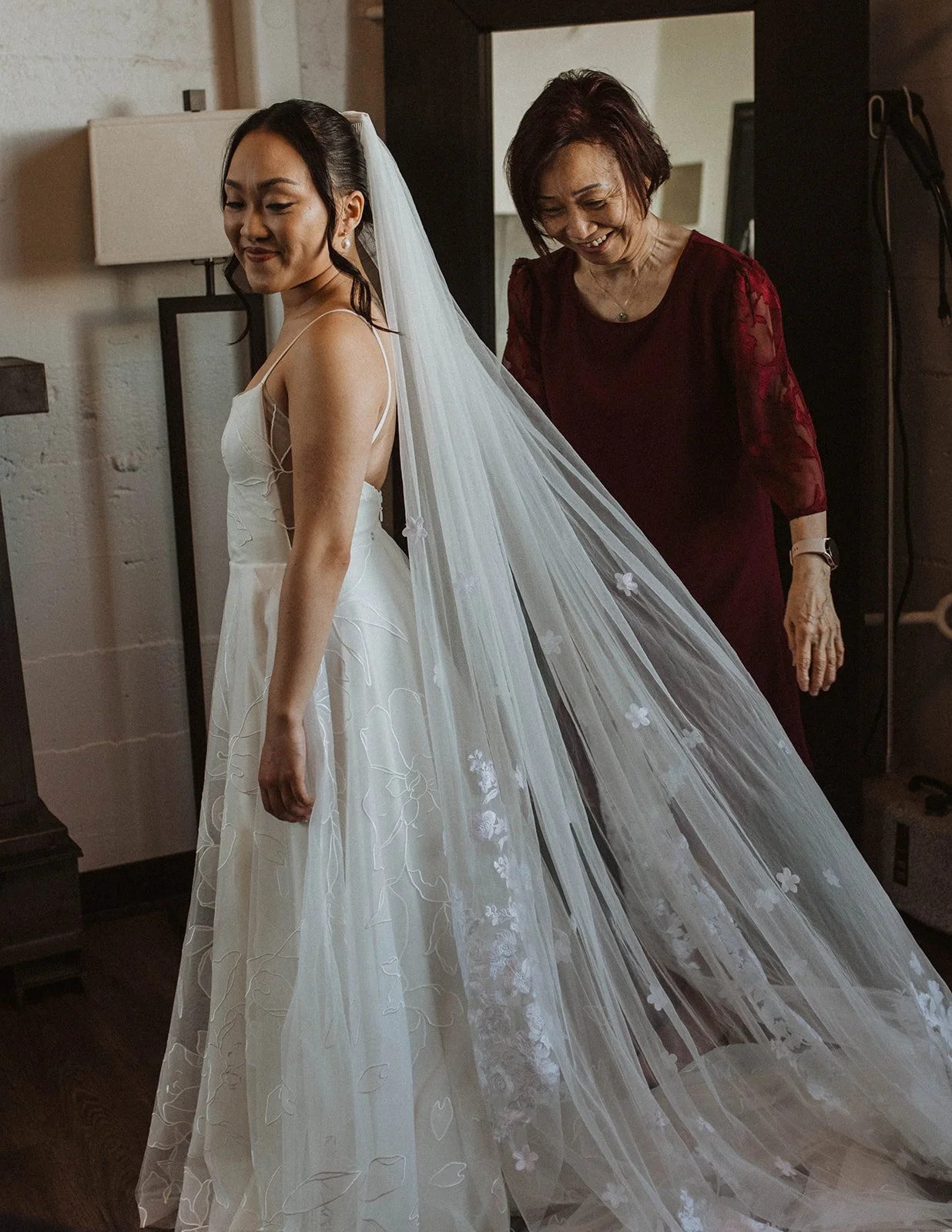 Bride smiles as her mother adjusts her veil while getting ready before a wedding at The Castaway in Portland.