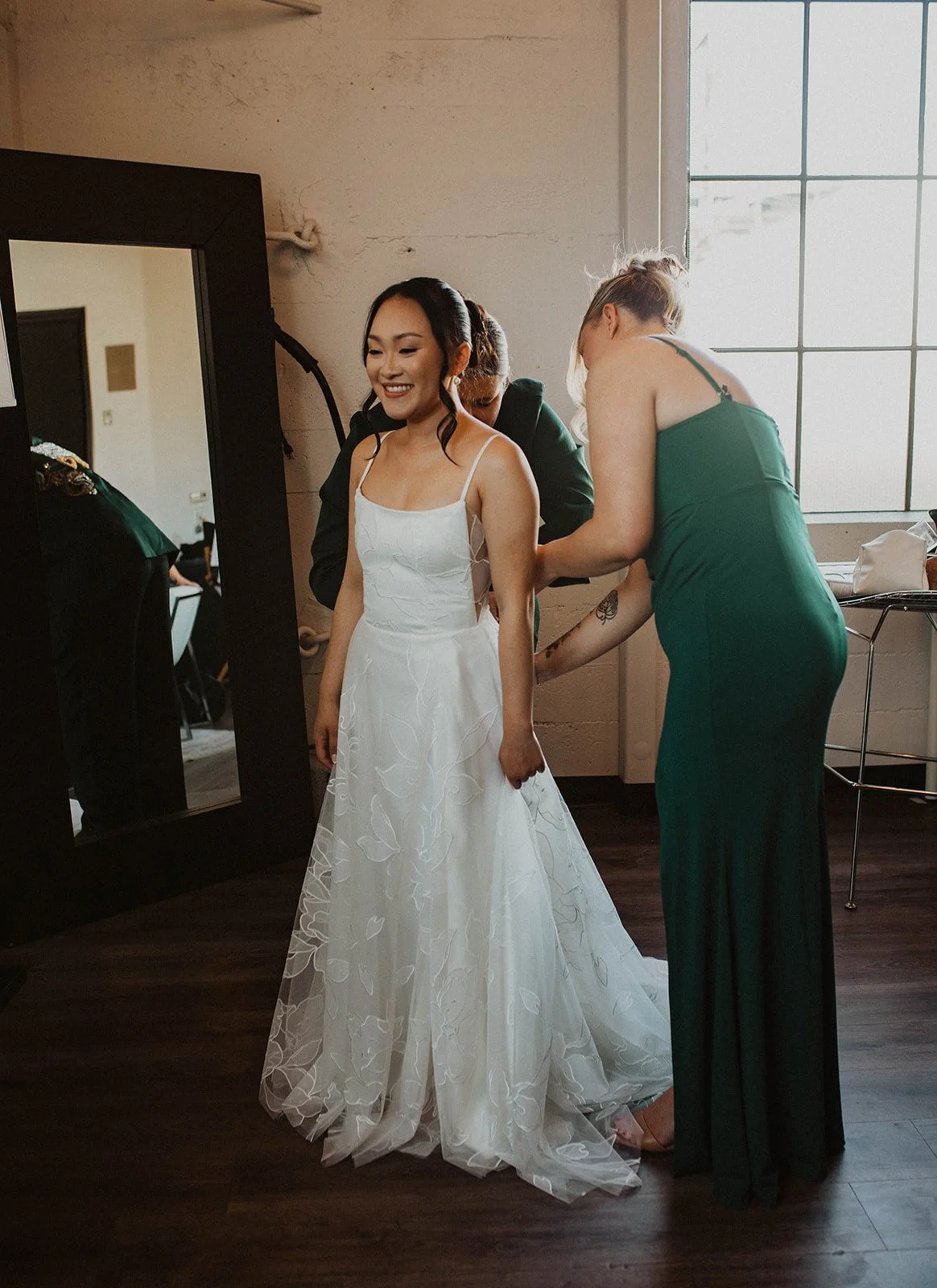 Bridesmaids help the bride with final dress adjustments while getting ready before a Portland wedding.
