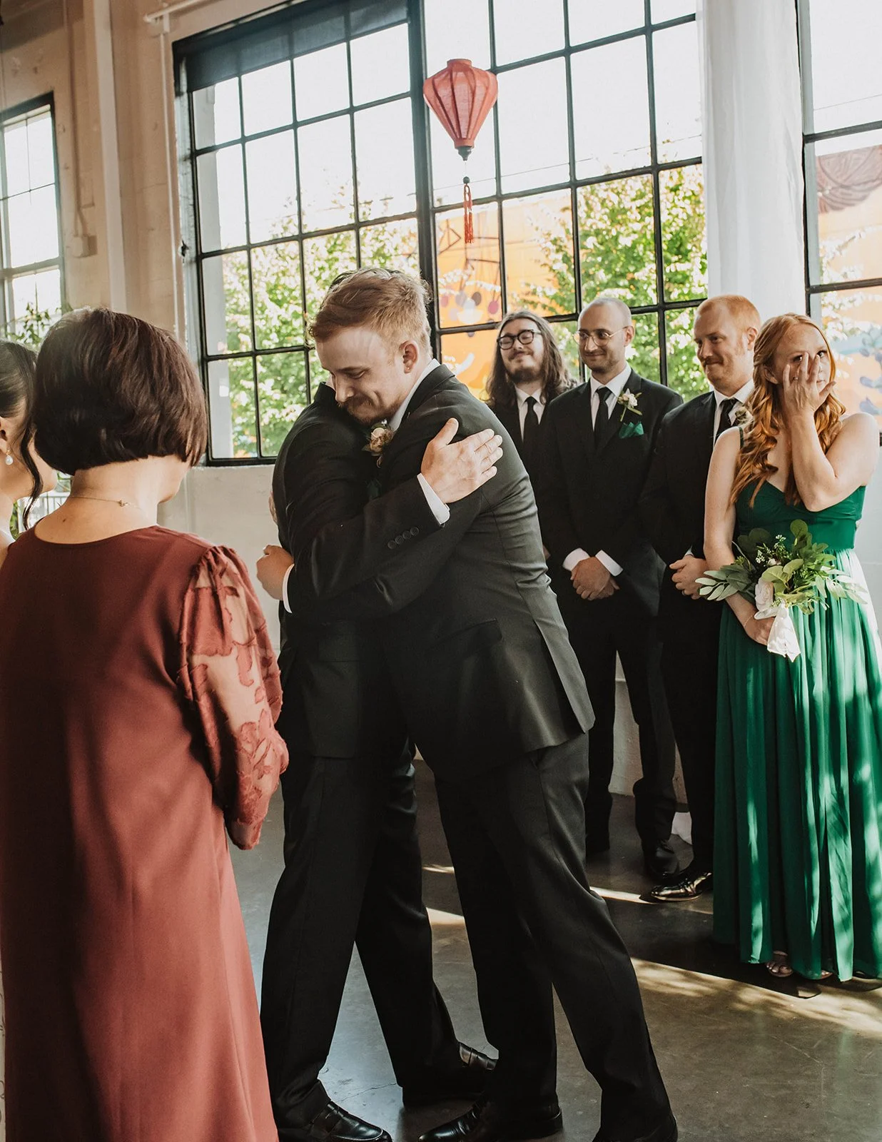Emotional moment during a Portland wedding ceremony as the groom shares a hug with a family member while wedding party members look on.