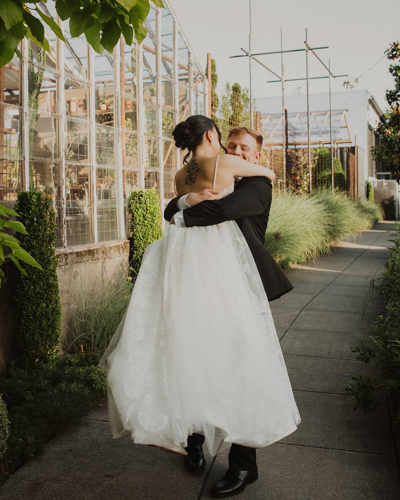 Groom lifts and spins his bride during joyful wedding portraits outside a greenhouse-inspired wedding venue.