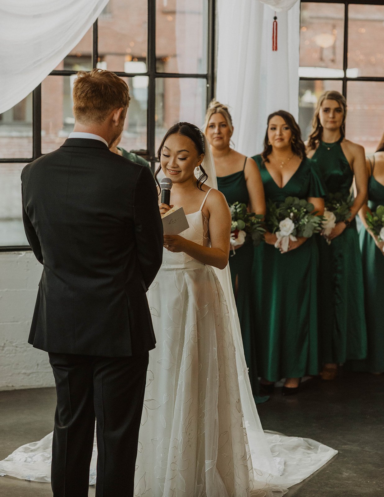 Bride reads personal wedding vows to her partner during an intimate Portland wedding ceremony surrounded by bridesmaids in emerald green dresses.