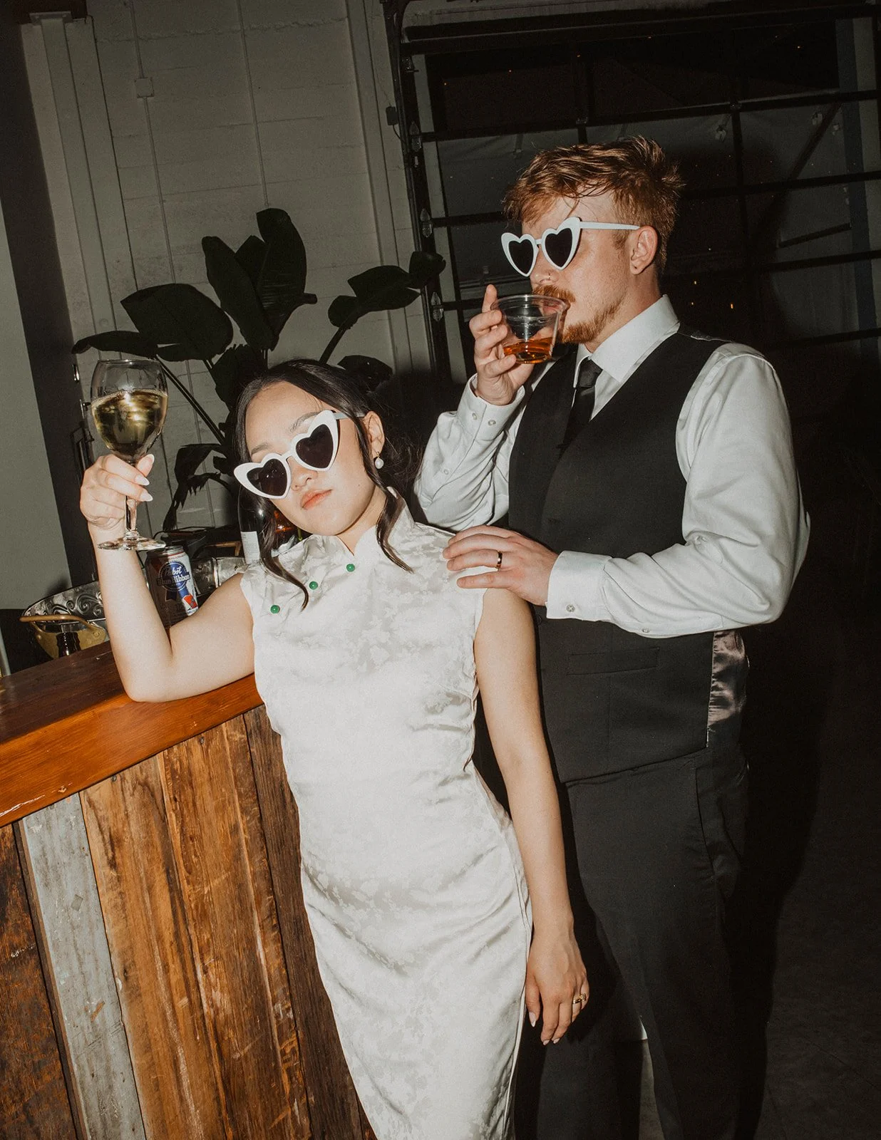 Bride and groom wearing heart-shaped sunglasses pose with drinks near the reception bar during their wedding celebration at The Castaway in Portland.