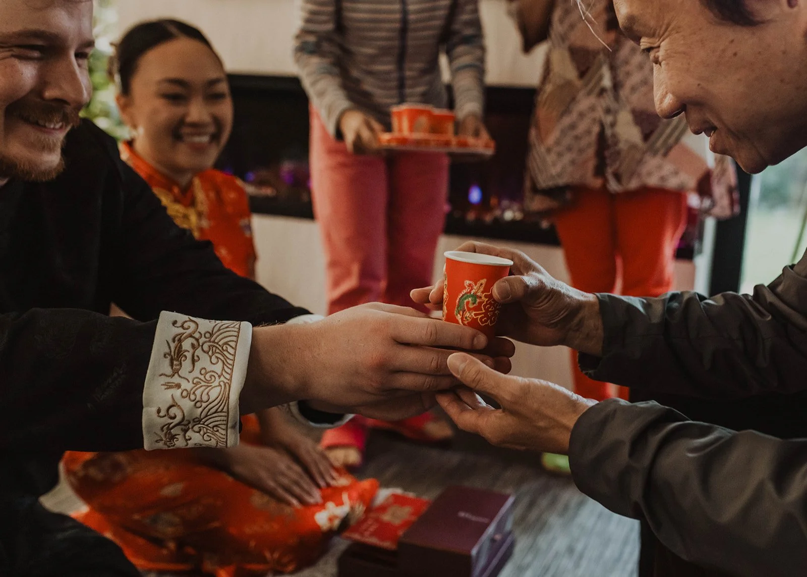 Groom presents a cup of tea to a family member during a traditional Chinese wedding tea ceremony while the bride smiles nearby.