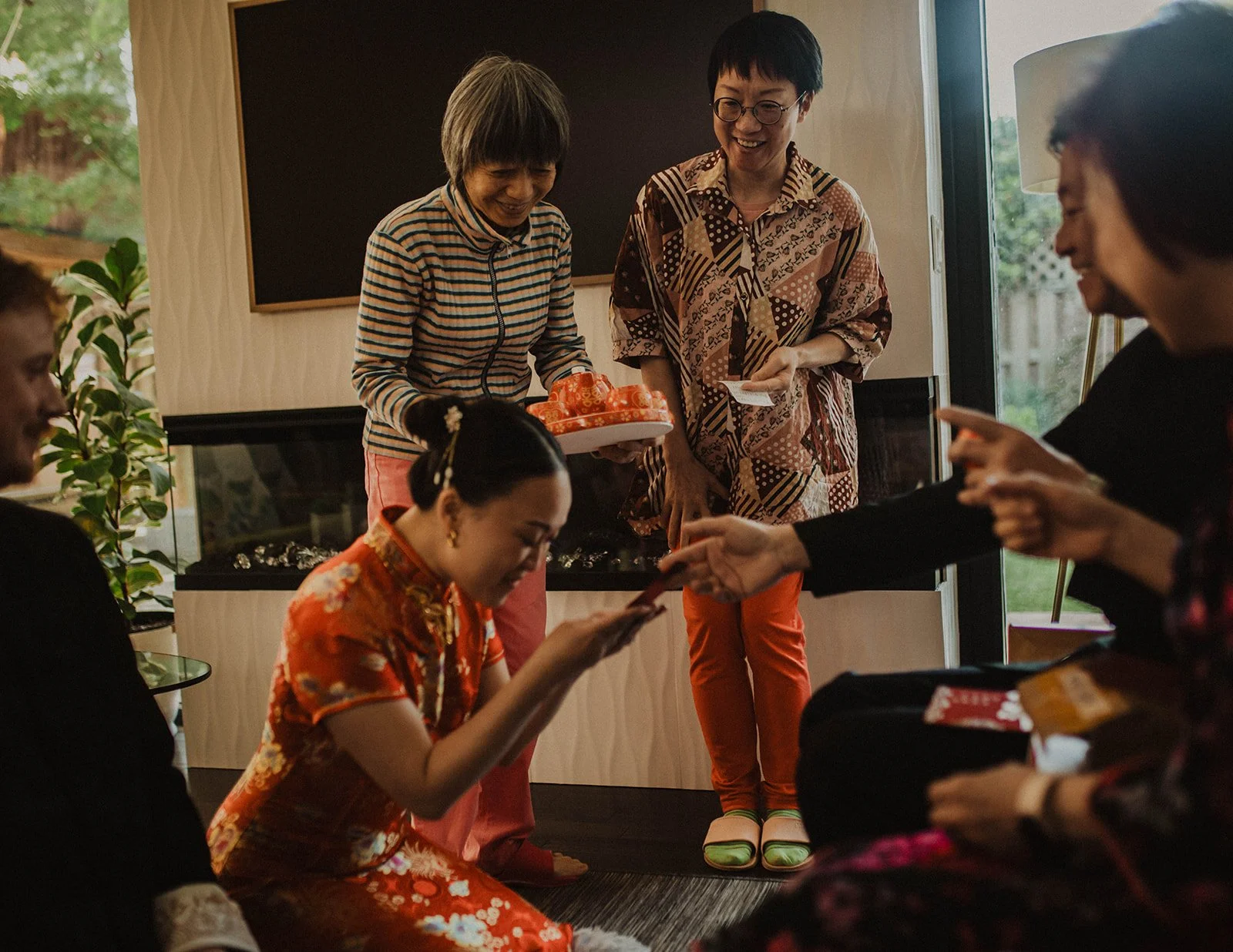 Bride kneels to receive a red envelope blessing from family members during a traditional Chinese wedding tea ceremony.