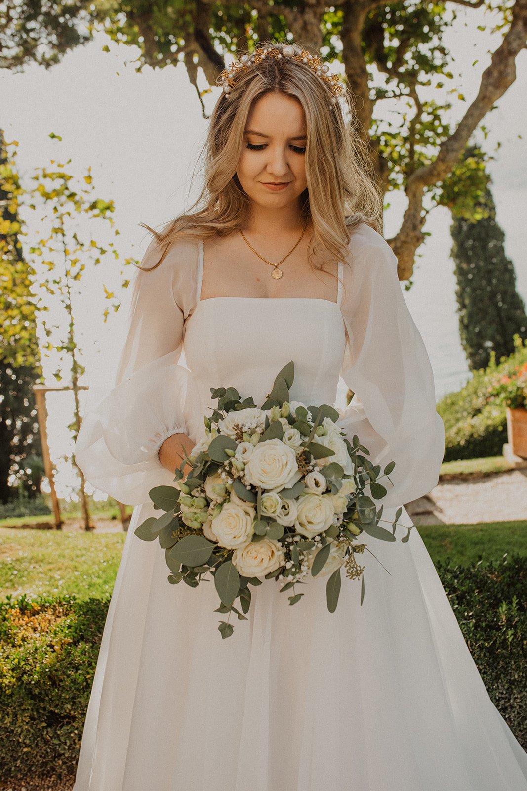 Bridal portrait at Villa del Balbianello featuring a modern wedding dress, white rose bouquet, and the gardens overlooking Lake Como.