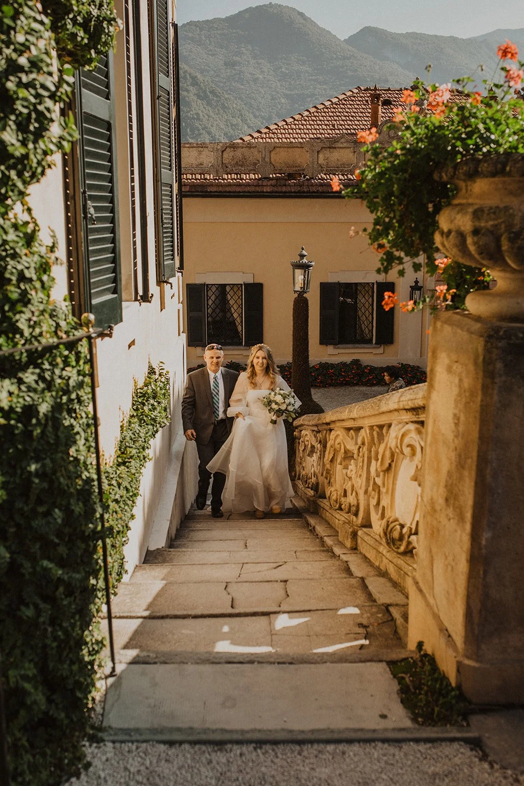 Bride walking with her father up the stone steps toward her intimate wedding ceremony at Villa del Balbianello on Lake Como.