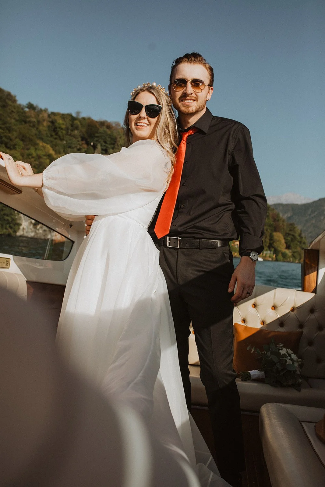 Newlyweds smiling together aboard a classic wooden boat during golden hour on Lake Como after their intimate wedding ceremony.