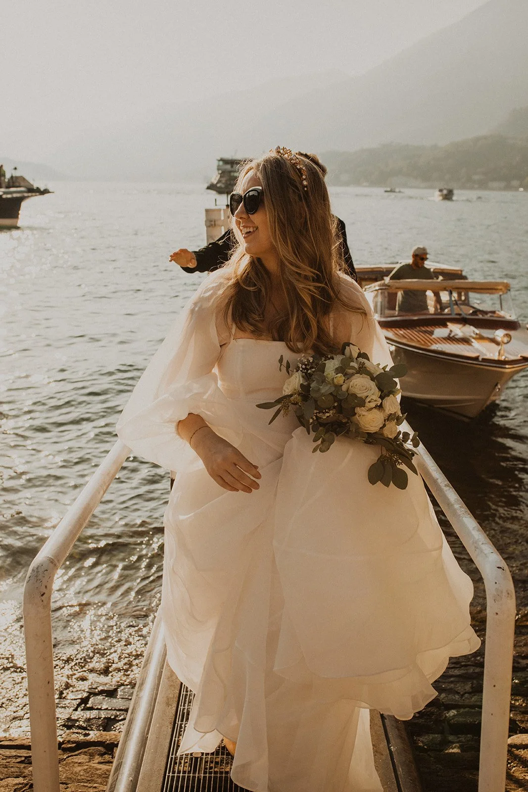 Bride carrying her bouquet while walking down the dock after arriving by boat on the shores of Lake Como.