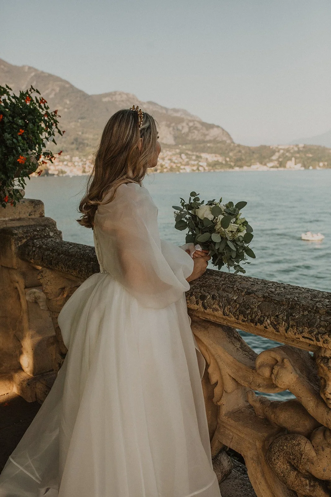 Bride overlooking Lake Como from the terrace at Villa del Balbianello while holding her bouquet before her intimate wedding ceremony in Italy.