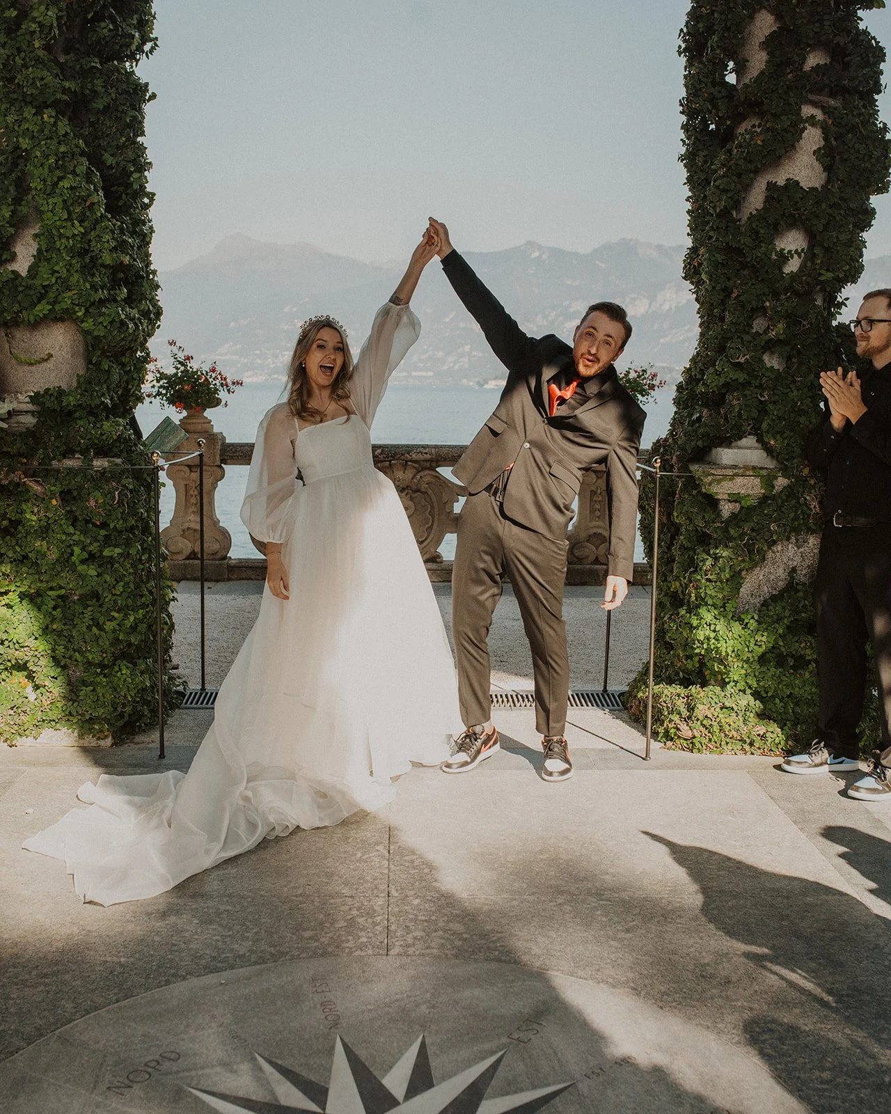 Newly married couple celebrating after their intimate ceremony at Villa del Balbianello overlooking Lake Como as guests applaud nearby.