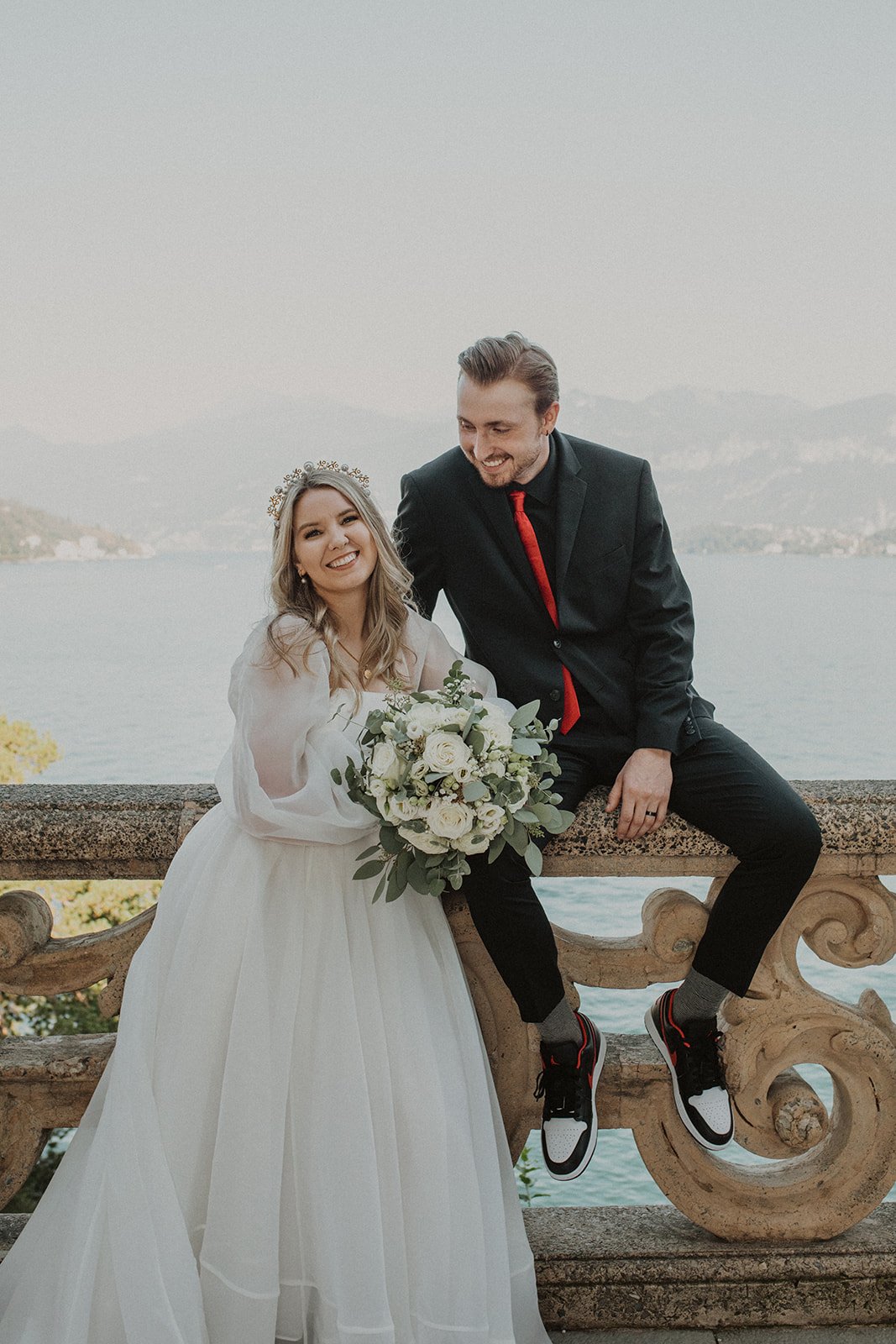 Bride and groom sitting together on the historic stone terrace at Villa del Balbianello during relaxed Lake Como wedding portraits.