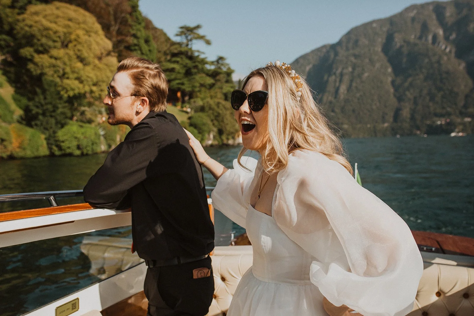 Newlyweds laughing together aboard a classic wooden boat while cruising across Lake Como after their intimate wedding ceremony.