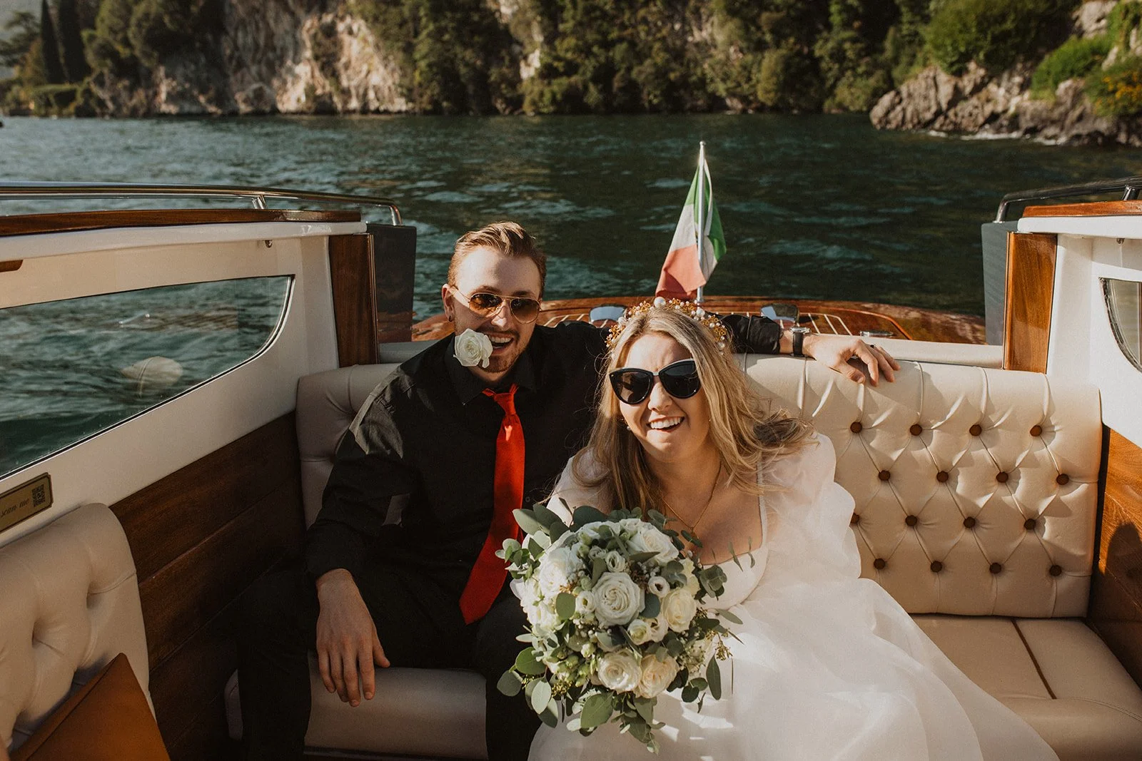 Bride and groom relaxing aboard a classic wooden boat with a white rose bouquet during their Lake Como elopement portraits.