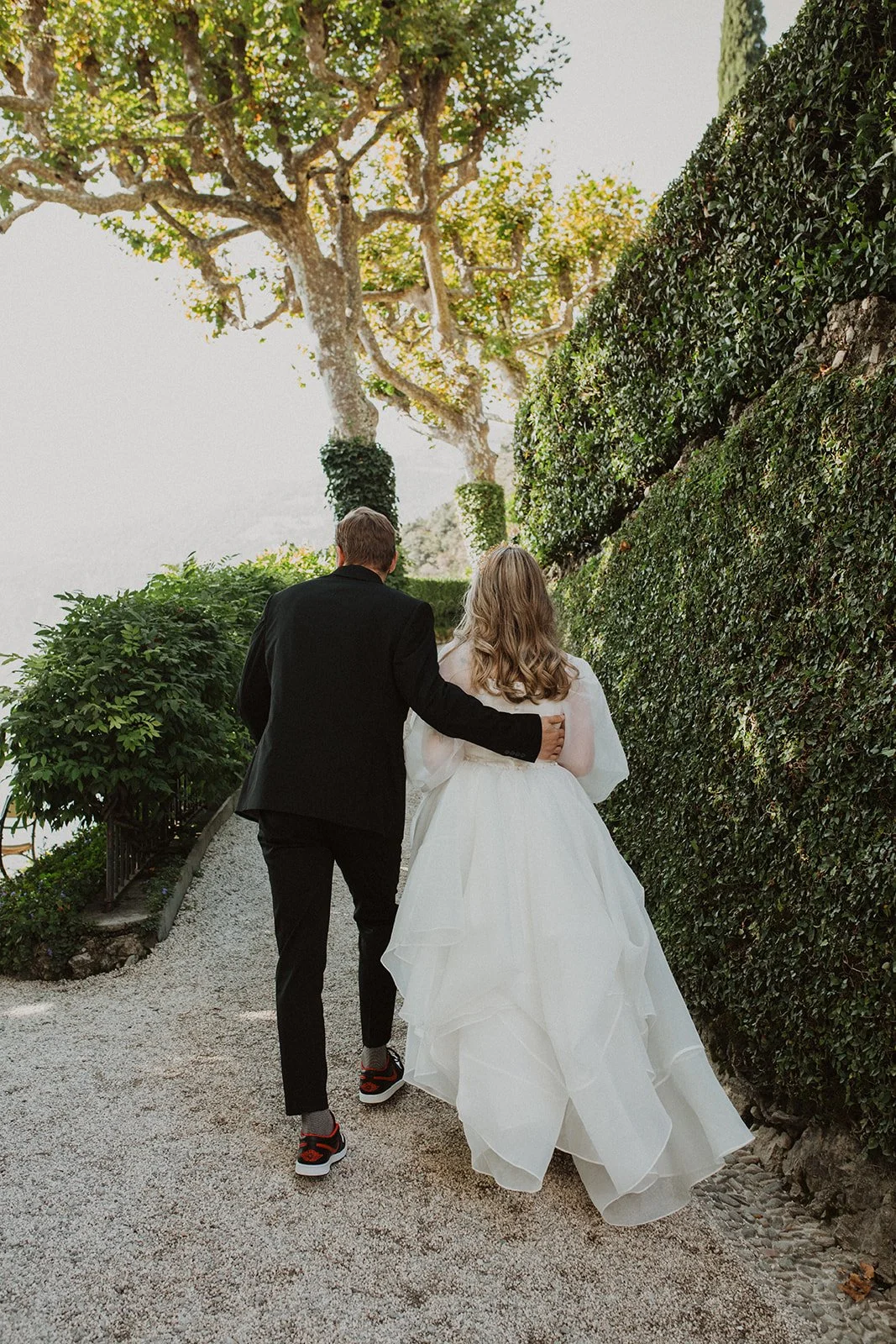 Newly married couple walking arm in arm through the manicured gardens of Villa del Balbianello after their Lake Como elopement.