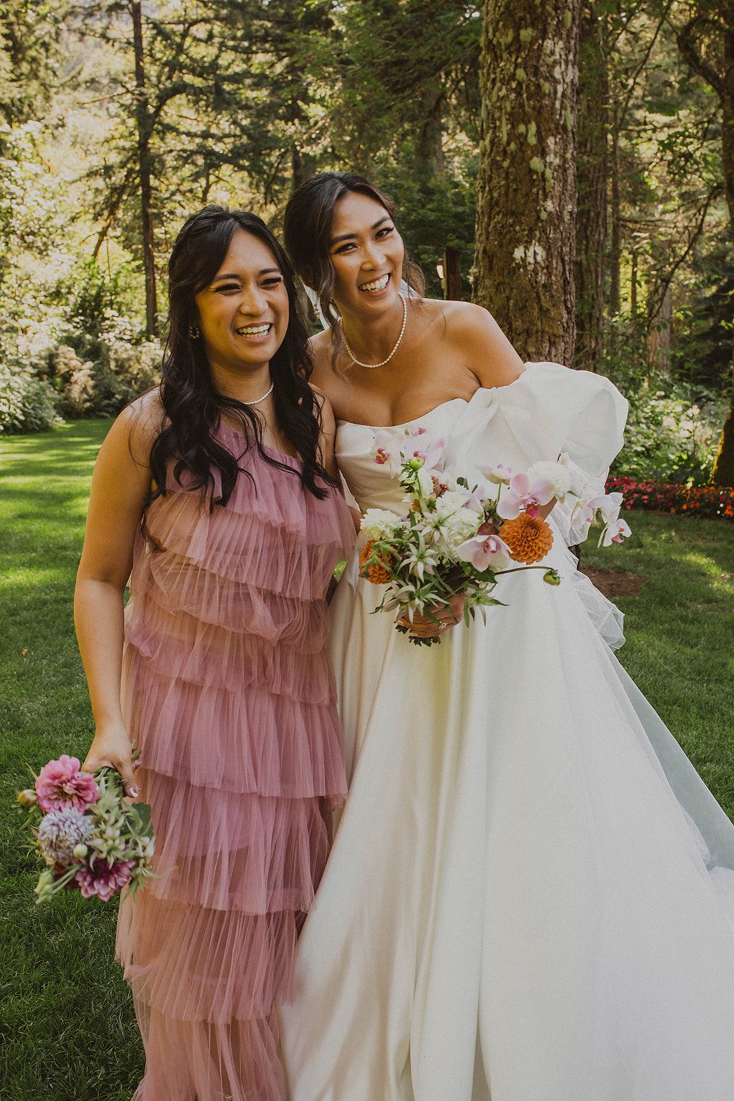 Bride smiling with her bridesmaid while holding colorful wedding bouquets during portraits at Bridal Veil Lakes in Oregon.