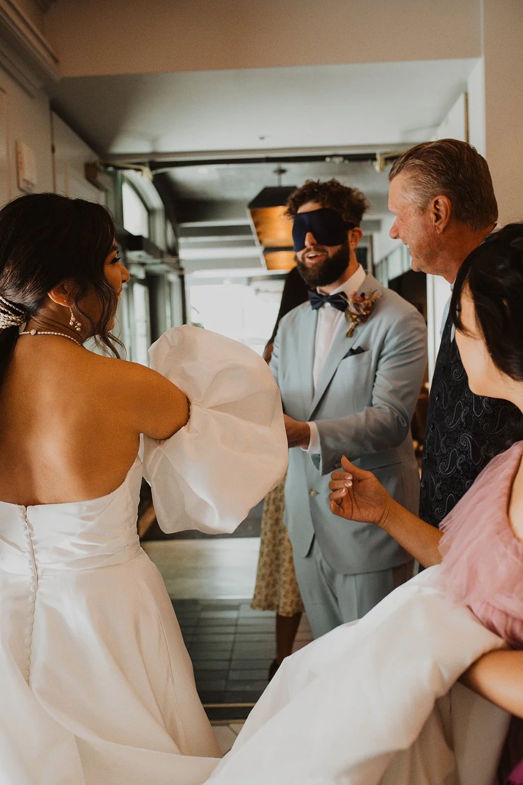Groom wearing a blindfold as family members prepare him for a surprise first look with his bride before their wedding at Bridal Veil Lakes.