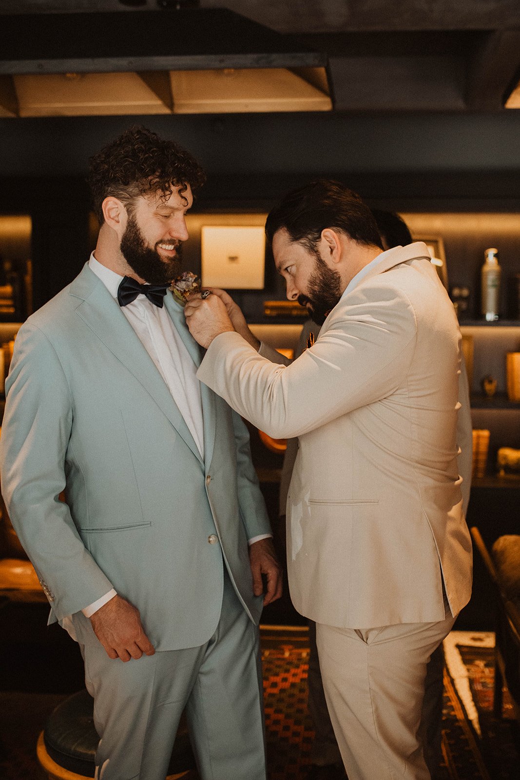 Groom smiling as a groomsman pins on his boutonniere during the getting-ready moments before the wedding ceremony at Bridal Veil Lakes.