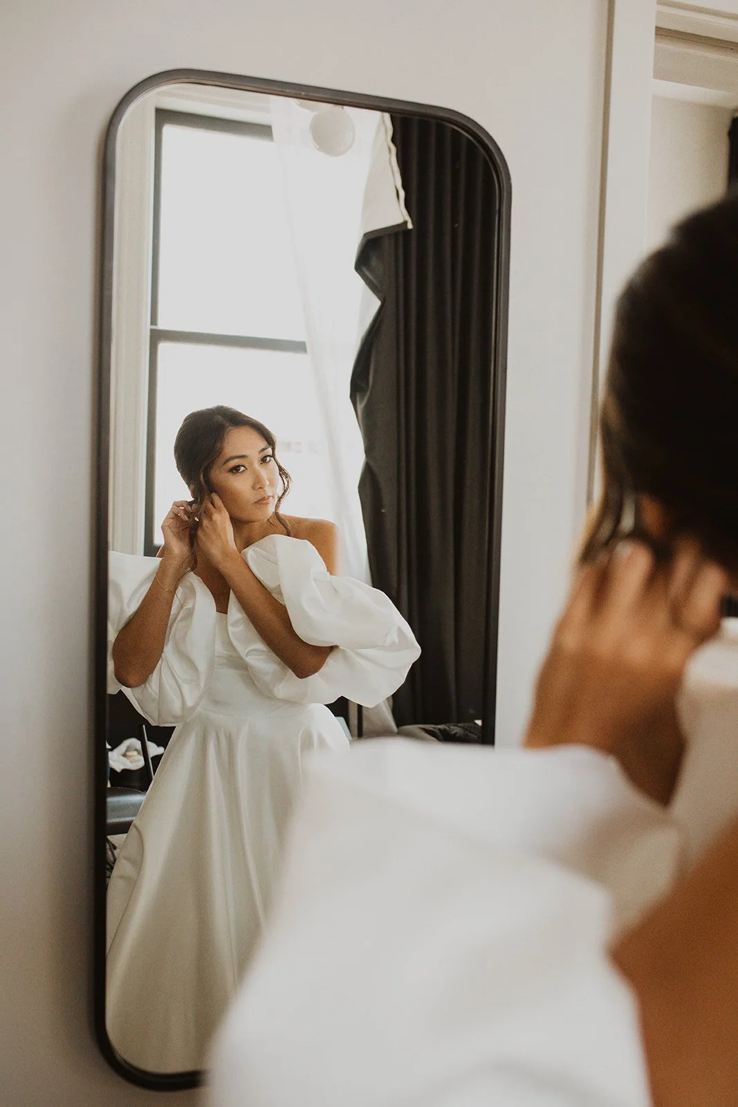 Bride adjusting her earrings in front of a mirror while getting ready for her wedding at Bridal Veil Lakes in Oregon.