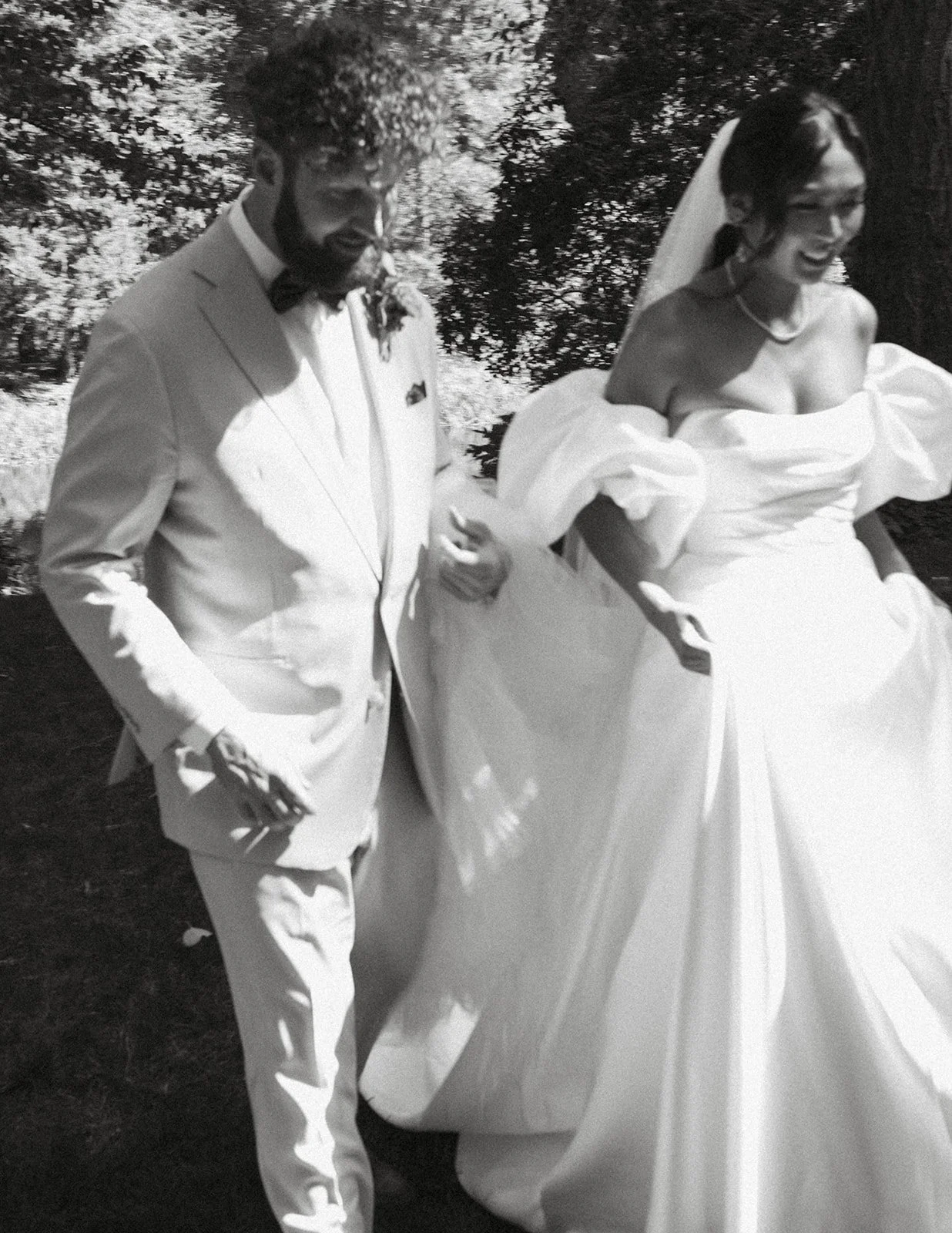 Black-and-white candid of the bride and groom walking together through the gardens at Bridal Veil Lakes after their wedding ceremony.