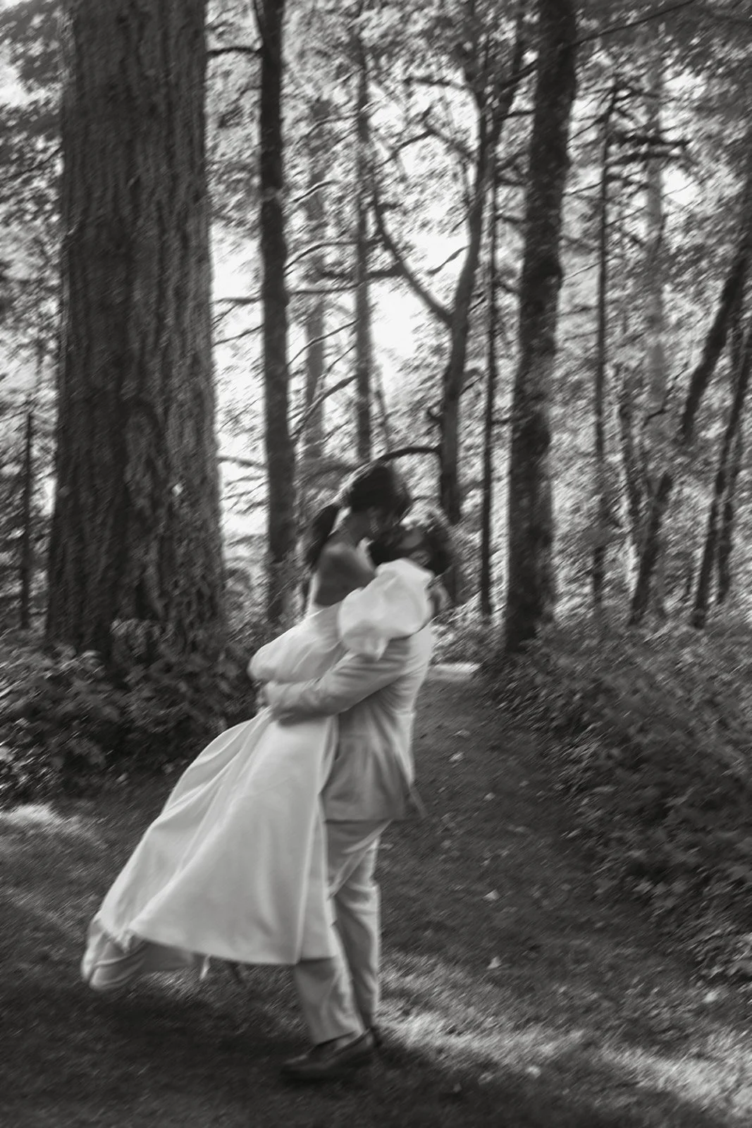 Black-and-white motion portrait of the groom dipping the bride for a kiss beneath towering trees at Bridal Veil Lakes wedding venue.