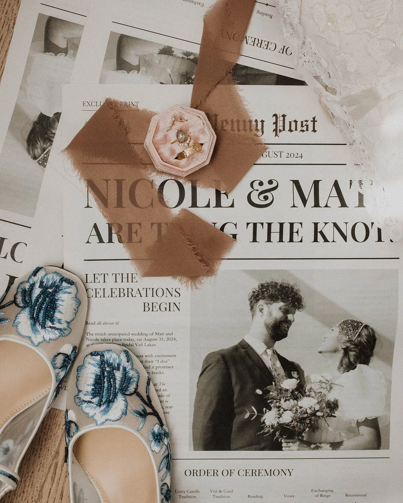 Wedding flat lay featuring embroidered bridal shoes, wedding rings, silk ribbon, lace veil, and a custom newspaper-style ceremony program at Bridal Veil Lakes.