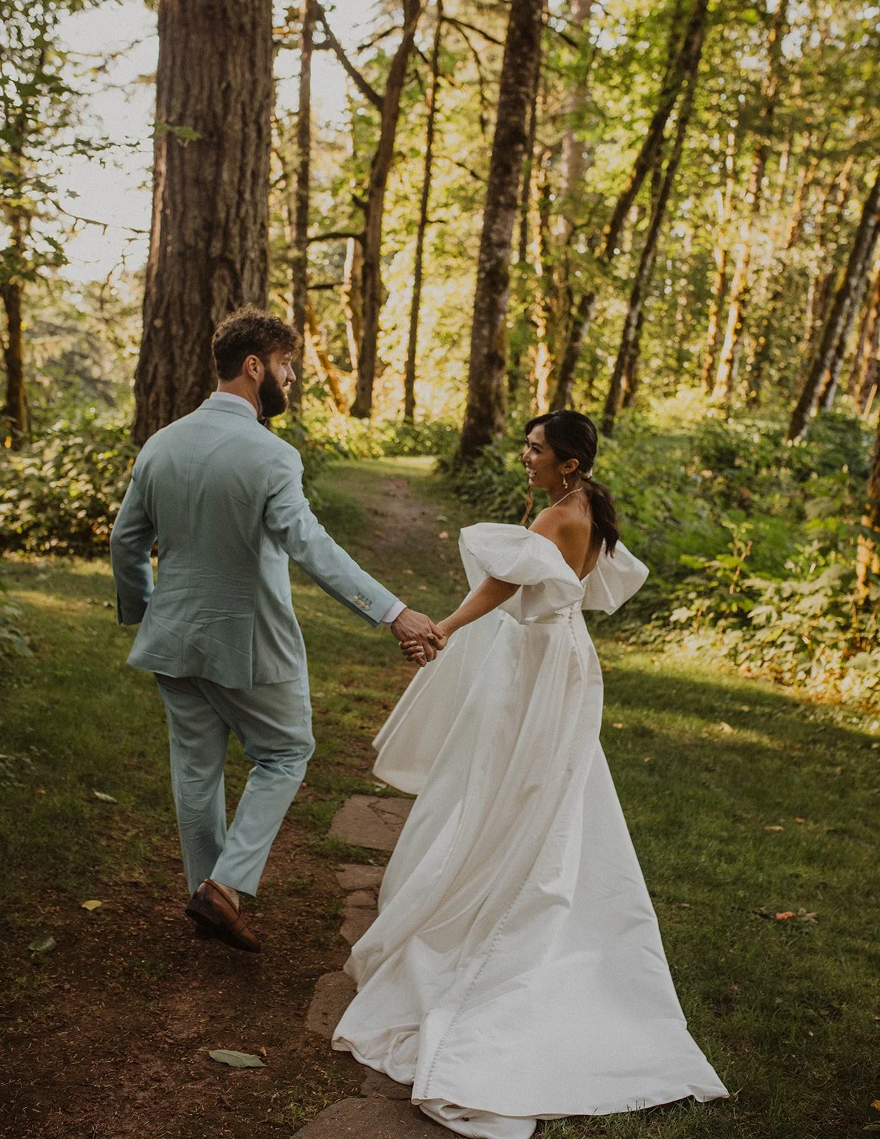 Bride and groom holding hands while walking along a forest path during golden hour wedding portraits at Bridal Veil Lakes.