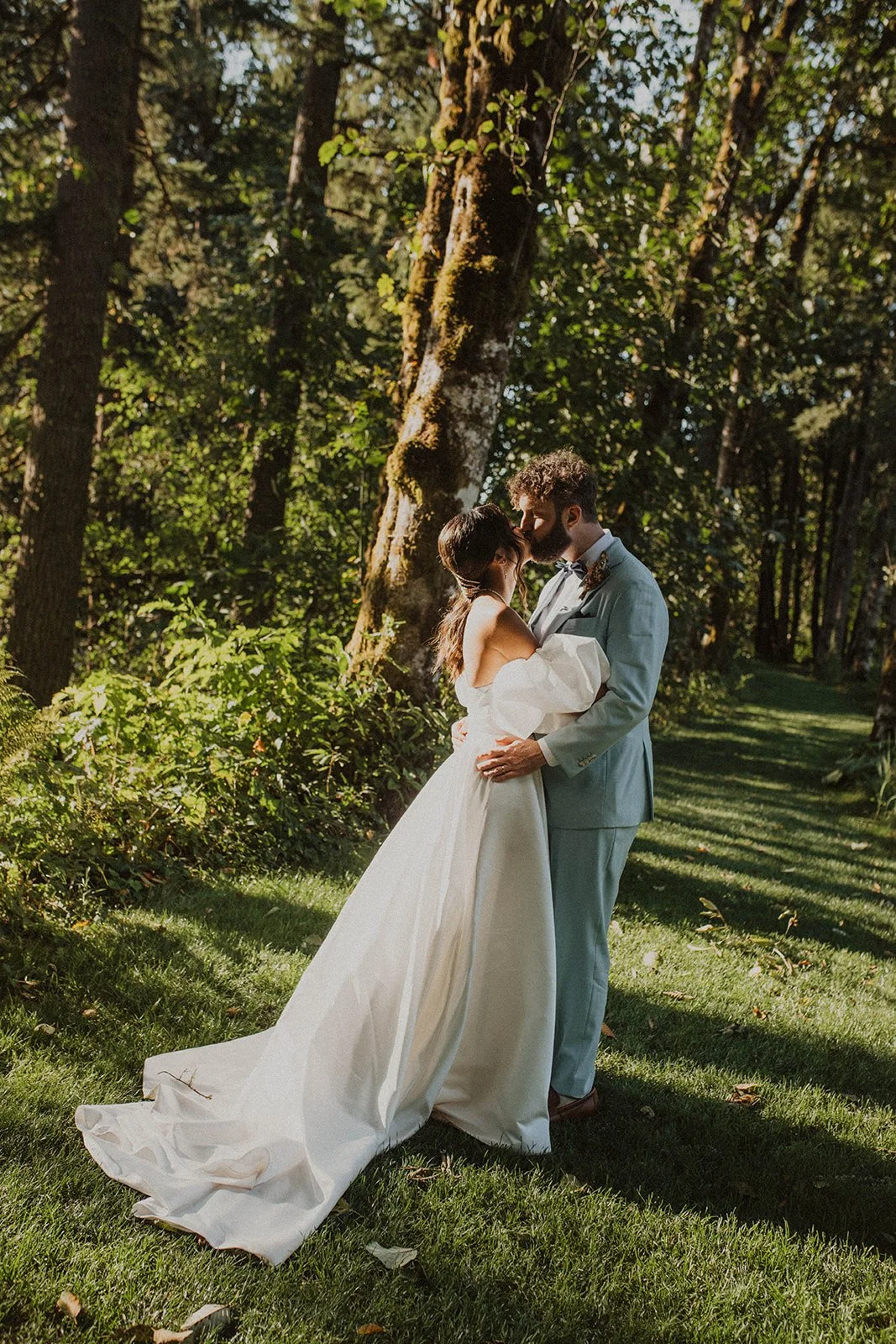 Bride and groom sharing a kiss beneath towering trees during forest wedding portraits at Bridal Veil Lakes.