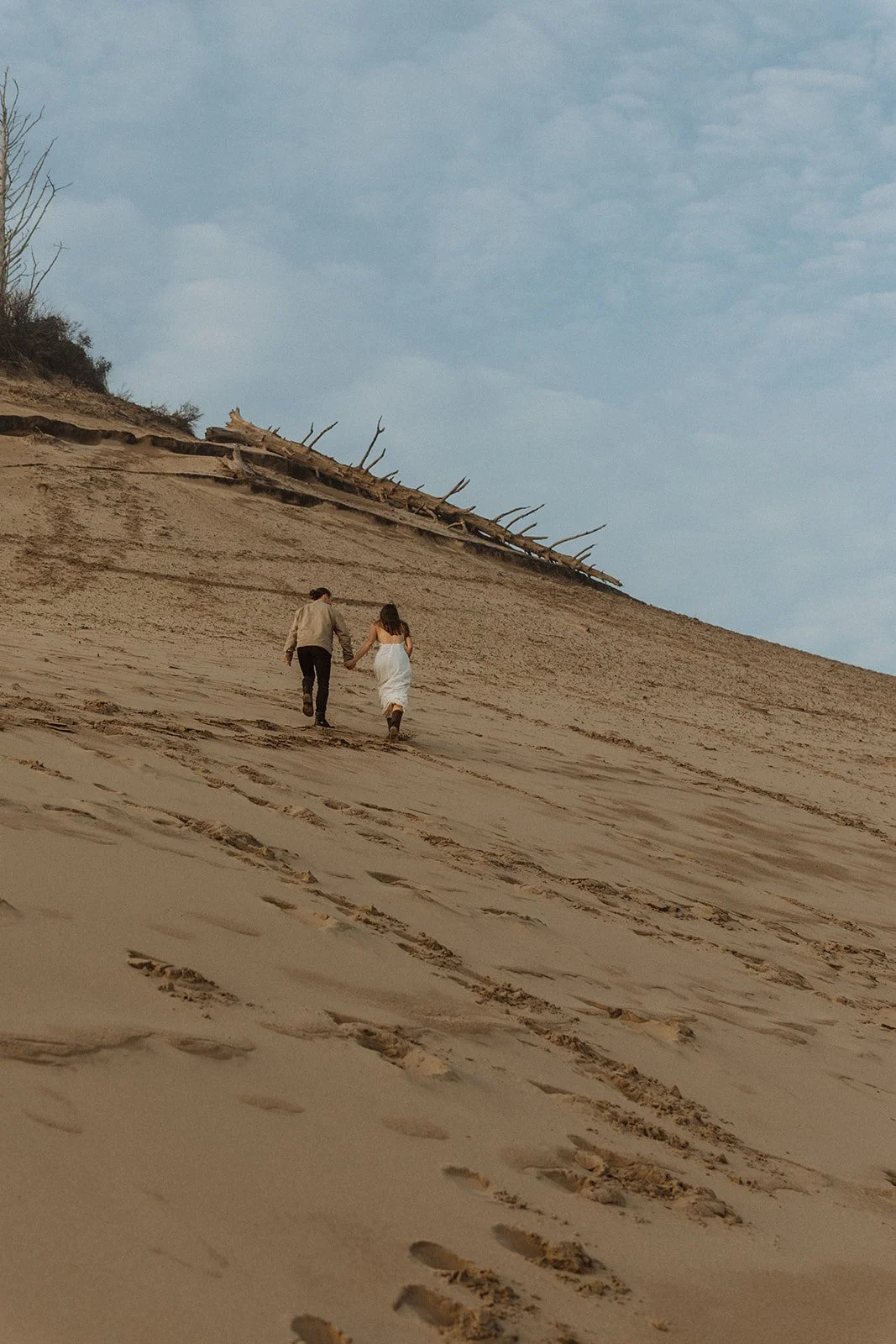 Couple hold hands while climbing one of the steep sand dunes at Cape Kiwanda