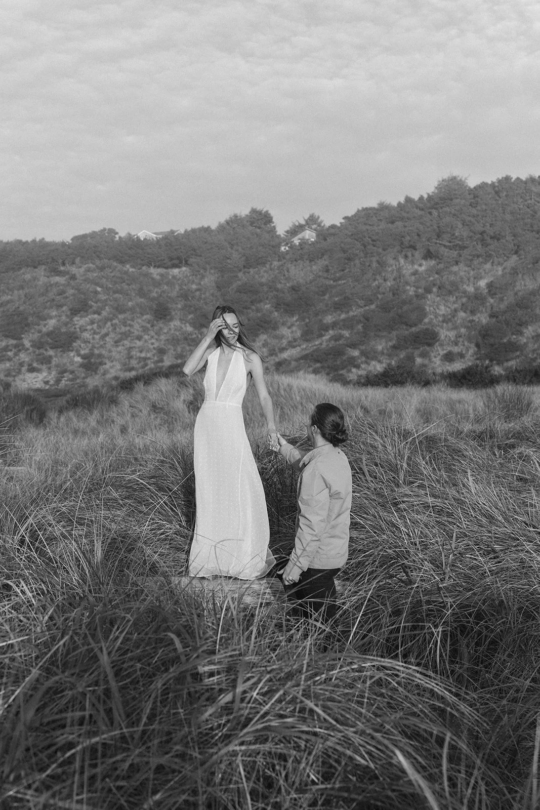 Lucas reaches for Miranda's hand as they stand among the coastal grasses during their Cape Kiwanda engagement session on the Oregon Coast