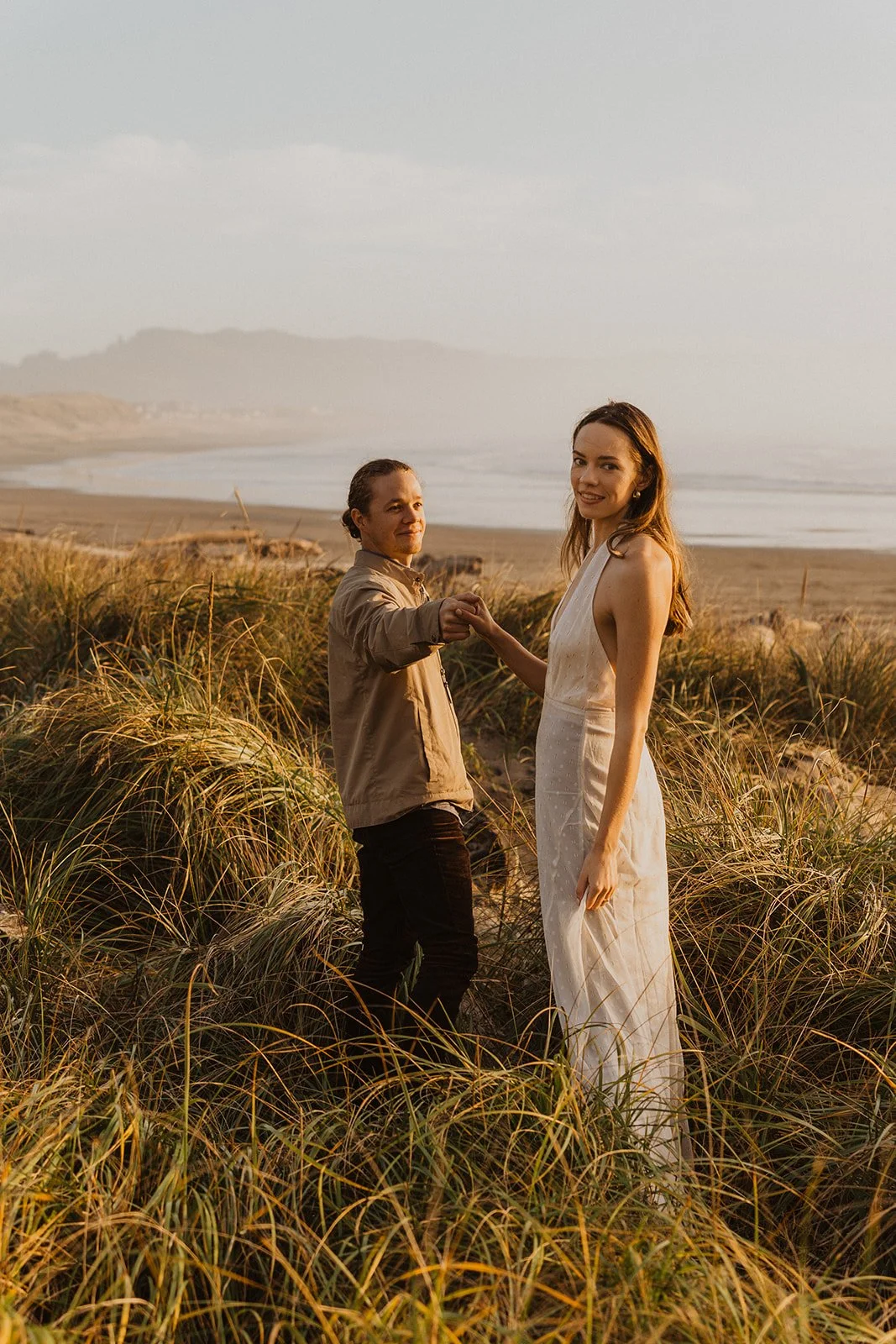 Couple hold hands in the beach grass overlooking the Oregon Coast during their Cape Kiwanda engagement session