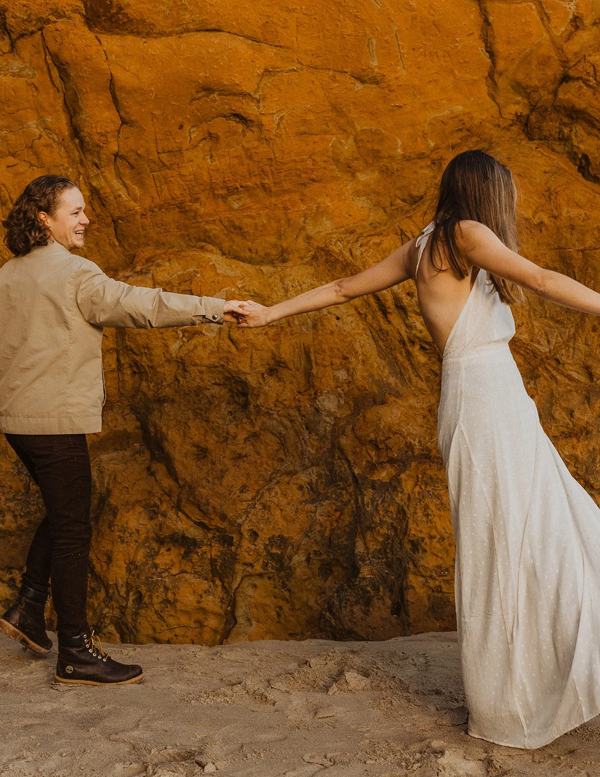 Miranda and Lucas hold hands beside the sandstone cliffs during their Cape Kiwanda engagement session.