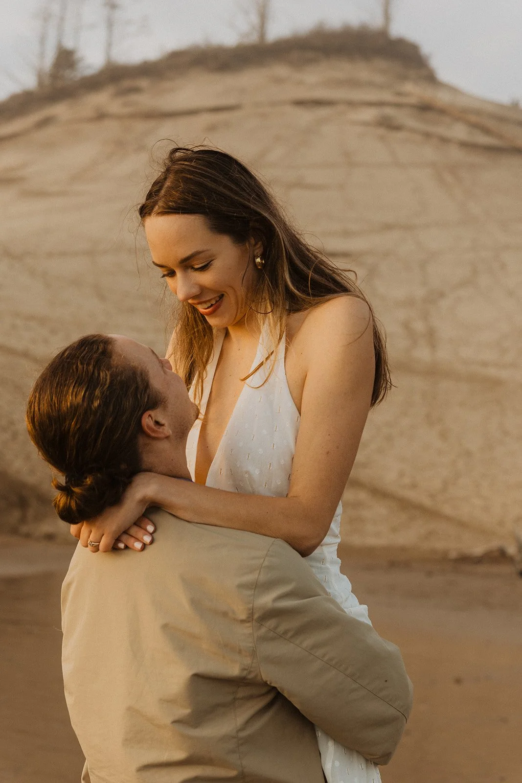 Couple smiles during golden hour while standing together on the beach at Cape Kiwanda during their Oregon Coast engagement session