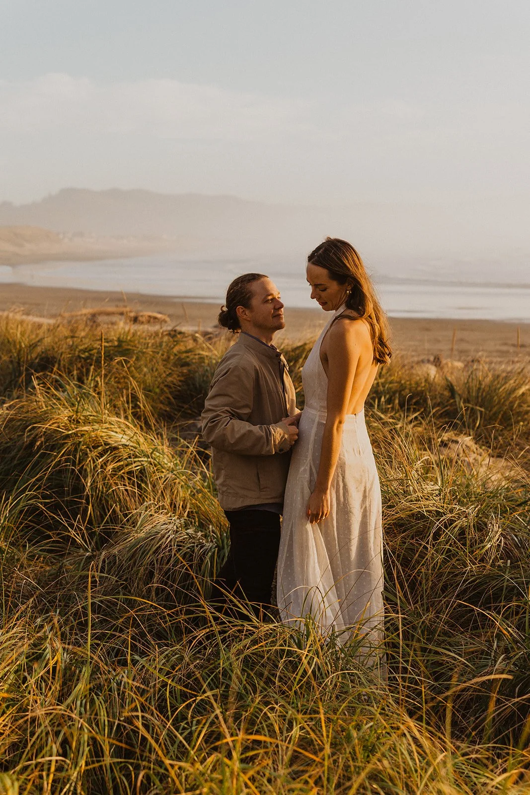 Couple romantically embrace on the Oregon shoreline with Haystack Rock in the background during their Cape Kiwanda engagement session