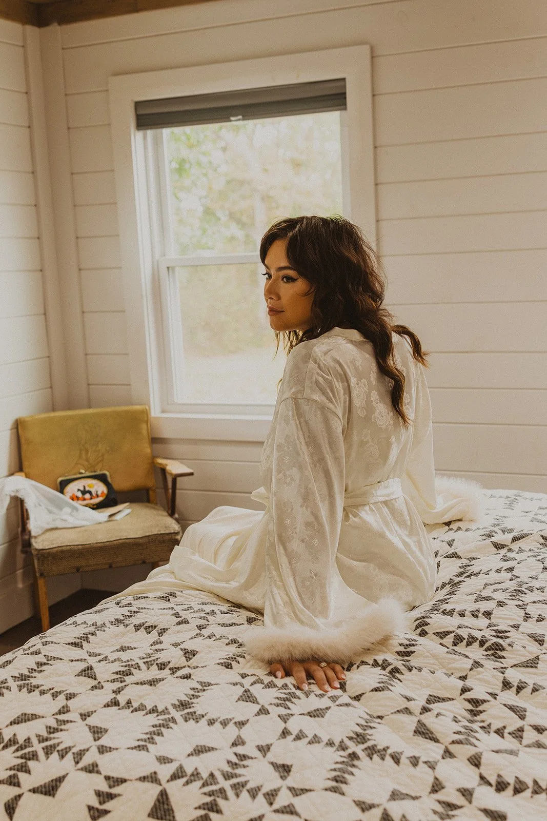 Bride wearing a satin bridal robe while sitting on the bed in the getting-ready suite at Bright Morning Farm.