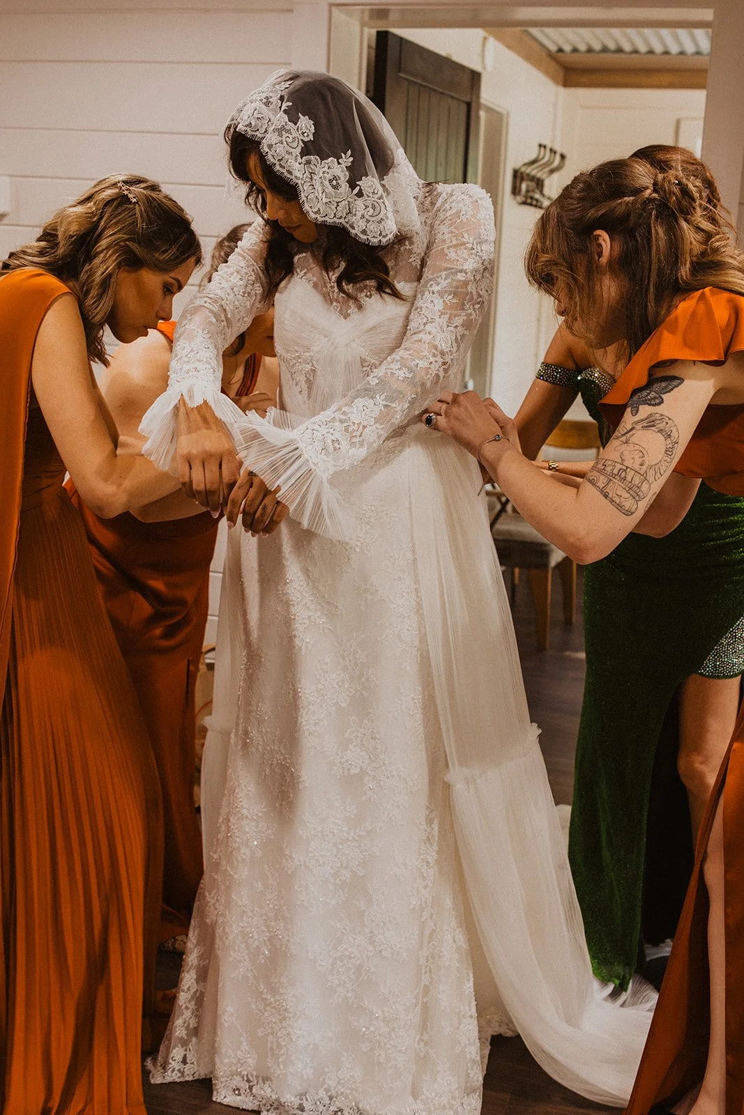 Bridesmaids helping the bride with the sleeves of her wedding dress while getting ready before the ceremony at Bright Morning Farm.