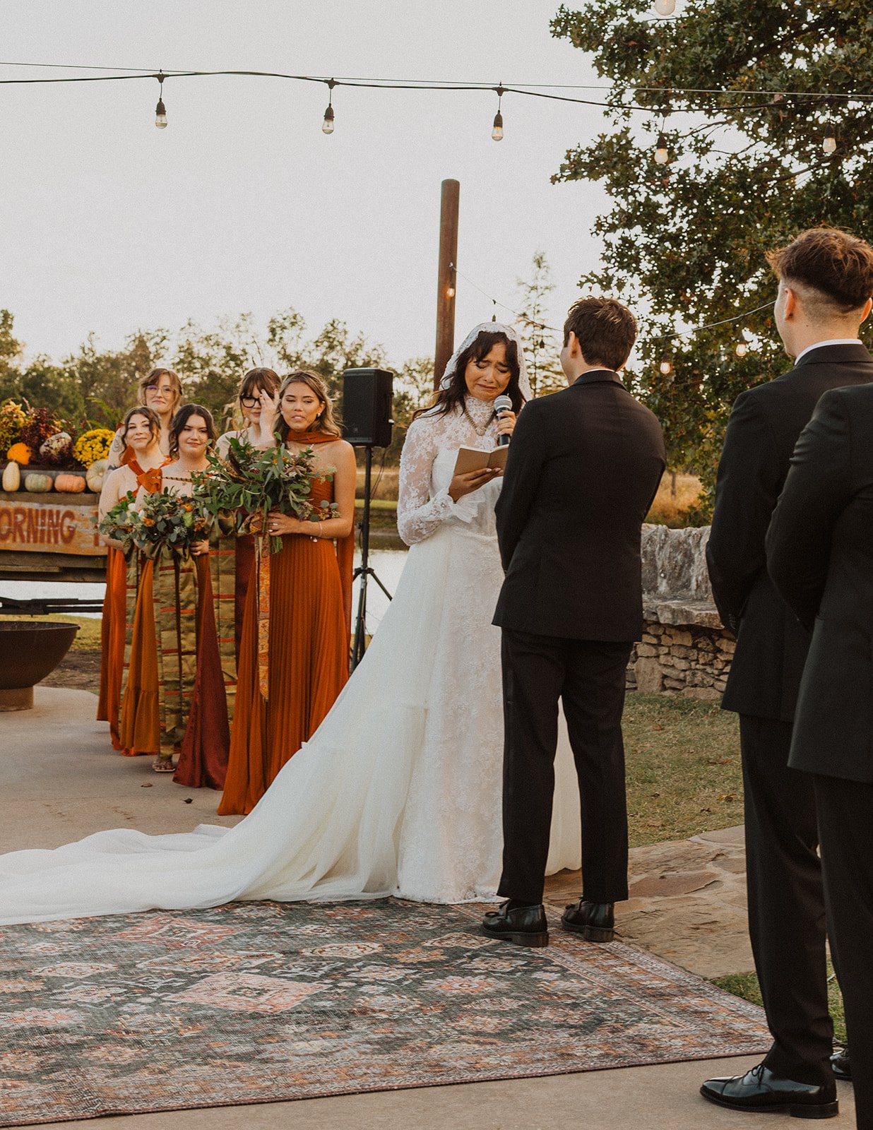 Bride reading her vows to the groom during an outdoor fall ceremony at Bright Morning Farm, with attendants in rust-colored dresses behind her.