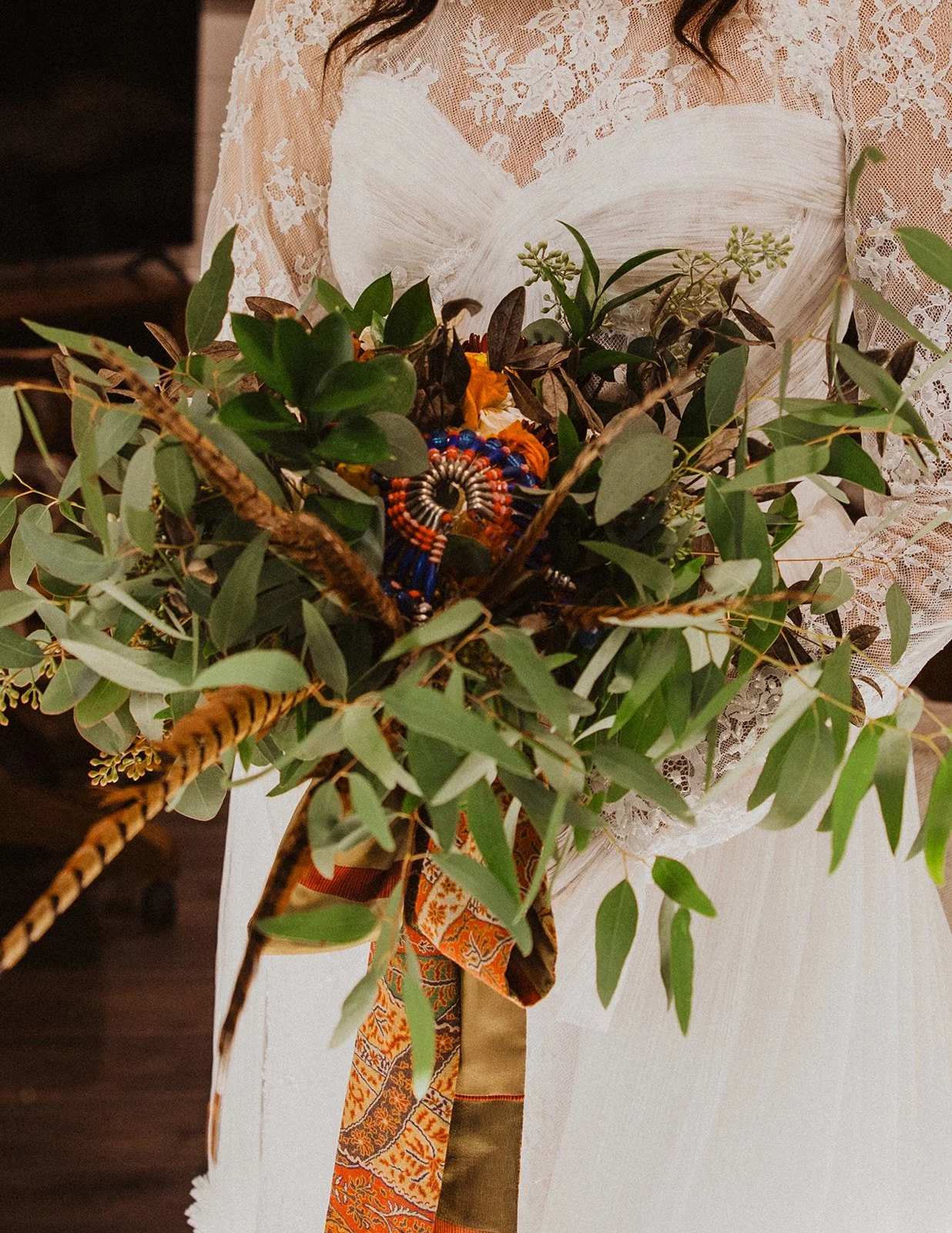 Close-up of the bride holding a fall wedding bouquet with eucalyptus, pheasant feathers, and patterned ribbon at Bright Morning Farm.