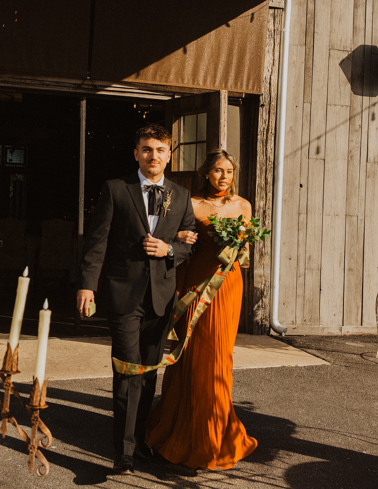 Wedding party members walking in the processional beside a wooden venue building during a fall wedding at Bright Morning Farm.