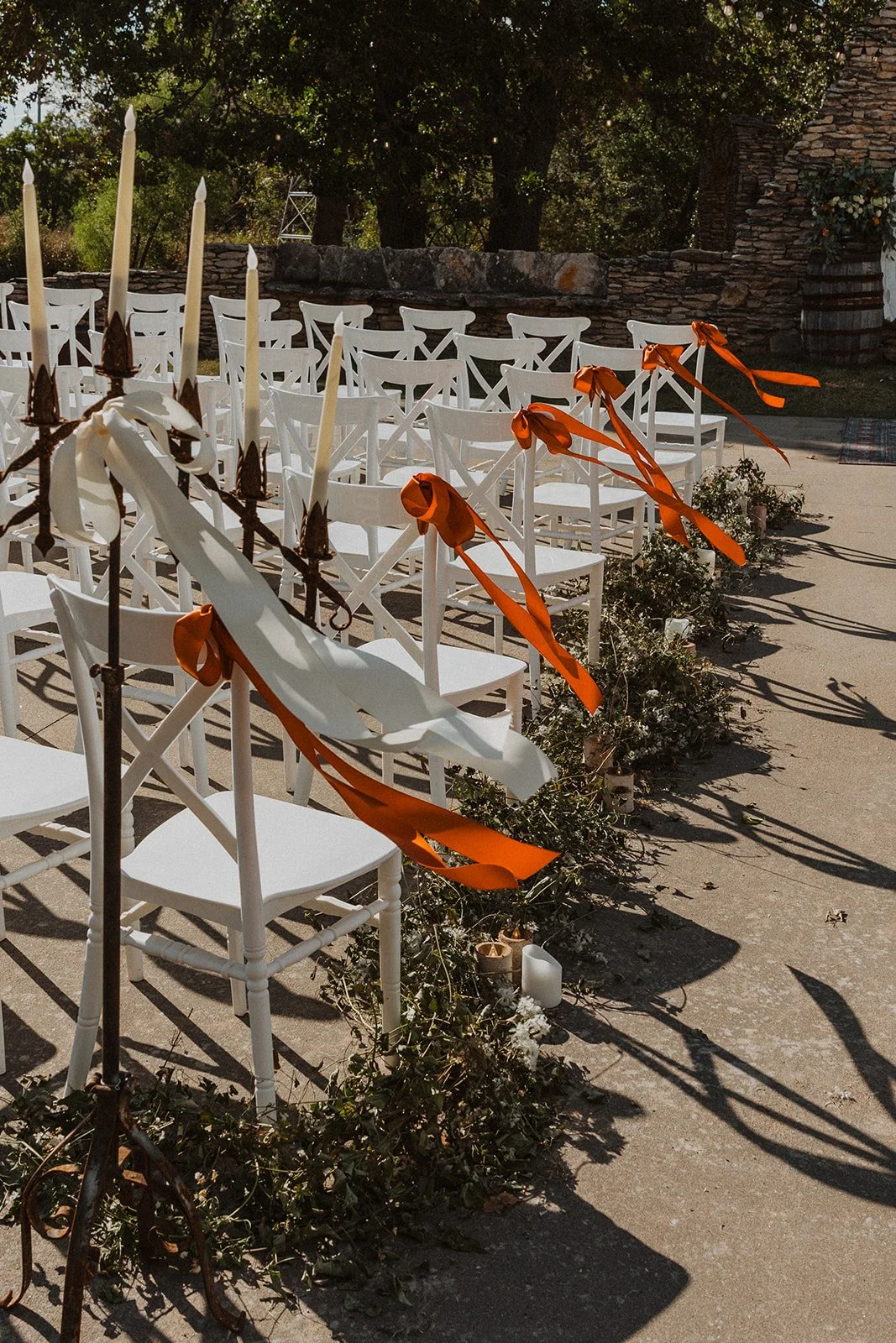 Outdoor wedding ceremony seating with white chairs, flowing orange ribbons, greenery, and candles at Bright Morning Farm.