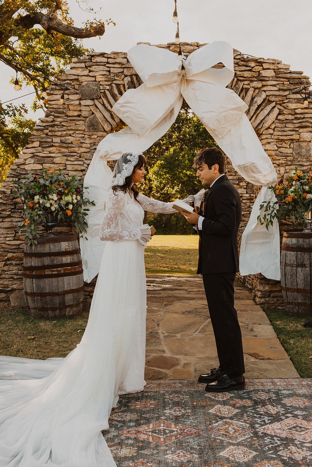 Bride placing her hand on the groom's shoulder while he reads his vows beneath the stone ceremony arch at Bright Morning Farm.