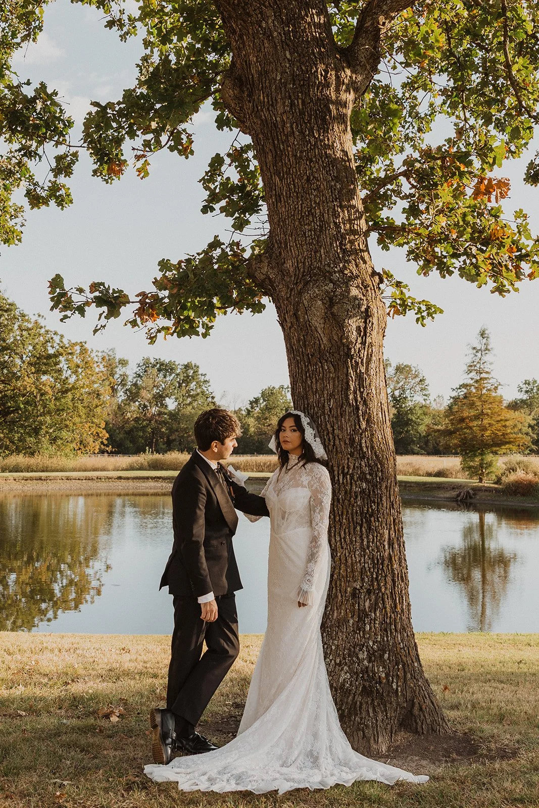 Bride and groom standing beneath a large oak tree beside the pond during wedding portraits at Bright Morning Farm.