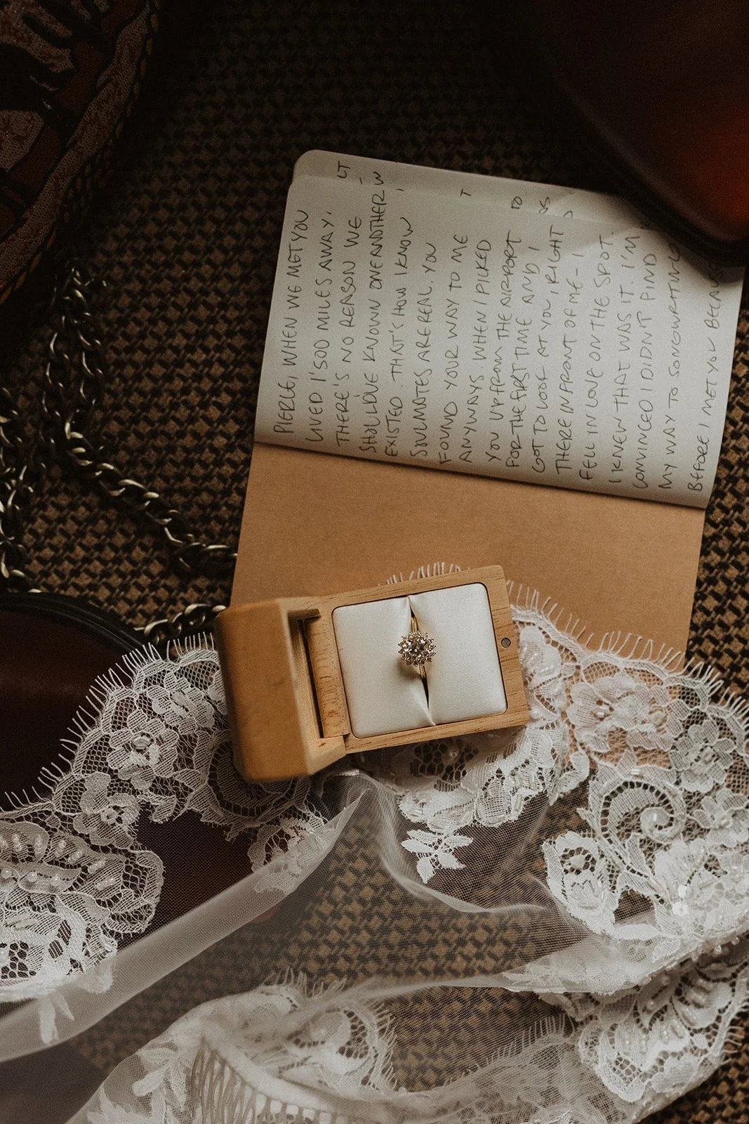 Bride's diamond engagement ring displayed in a wooden ring box beside a handwritten love letter and lace wedding veil