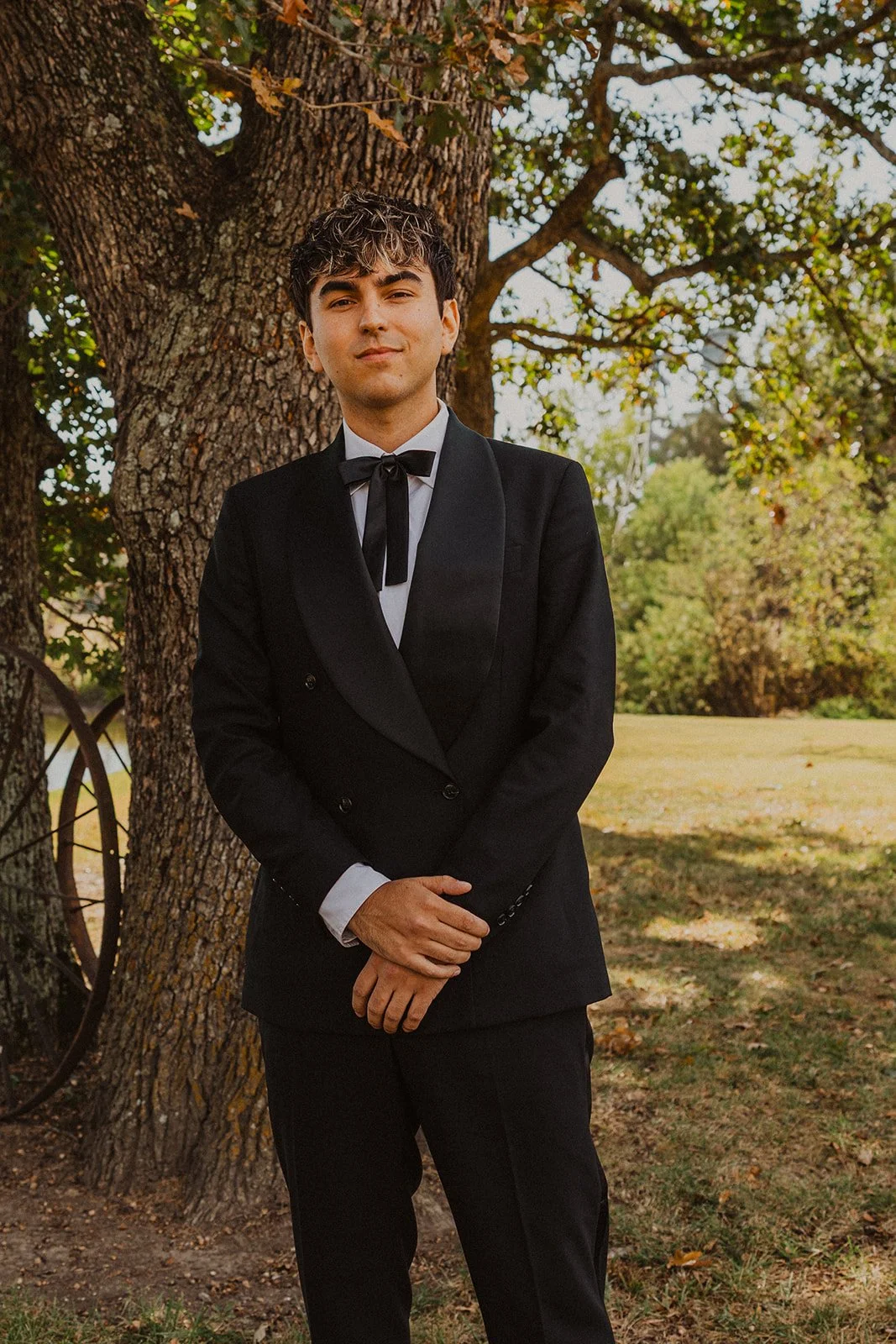 Portrait of the groom in a black tuxedo standing beneath a large oak tree before the ceremony at Bright Morning Farm.